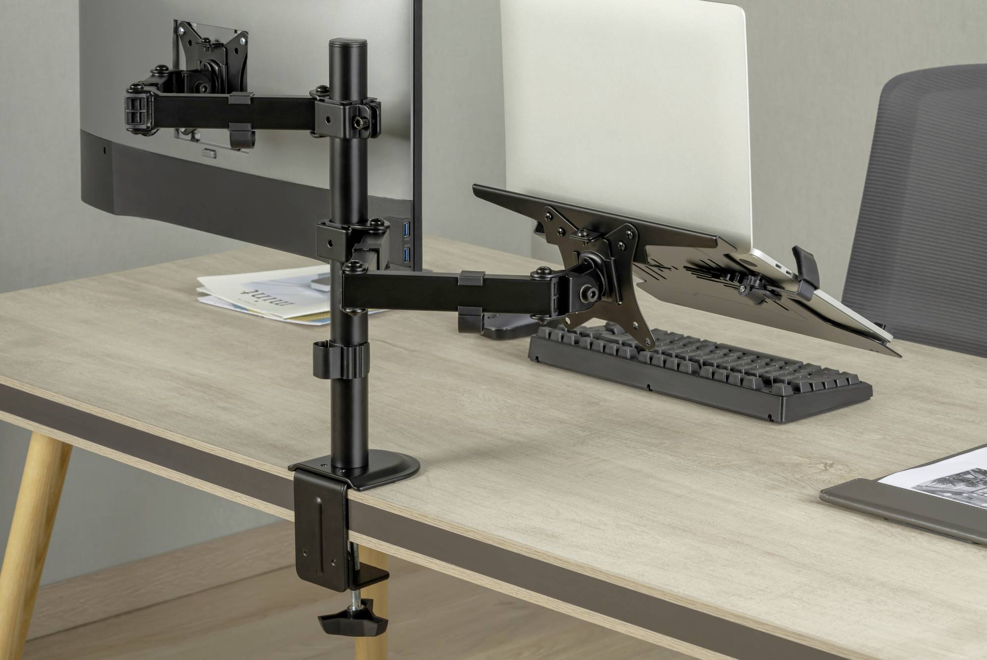 Biurko z dwoma monitorami na ramionach. Jeden wyświetla dokument, drugi jest pusty. Między nimi leży klawiatura.