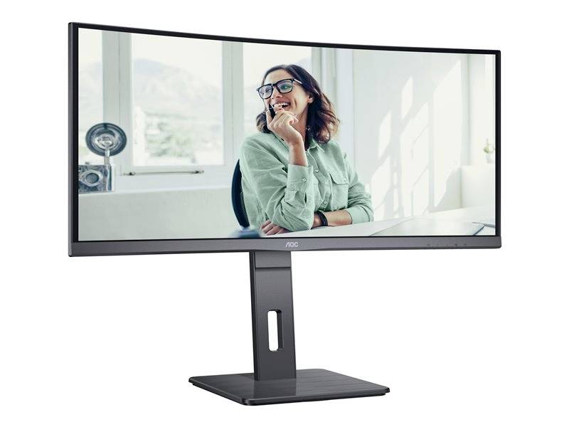 Uśmiechnięta osoba siedzi przy biurku, widoczna na dużym, zakrzywionym ekranie. Jasne, nowoczesne środowisko biurowe.