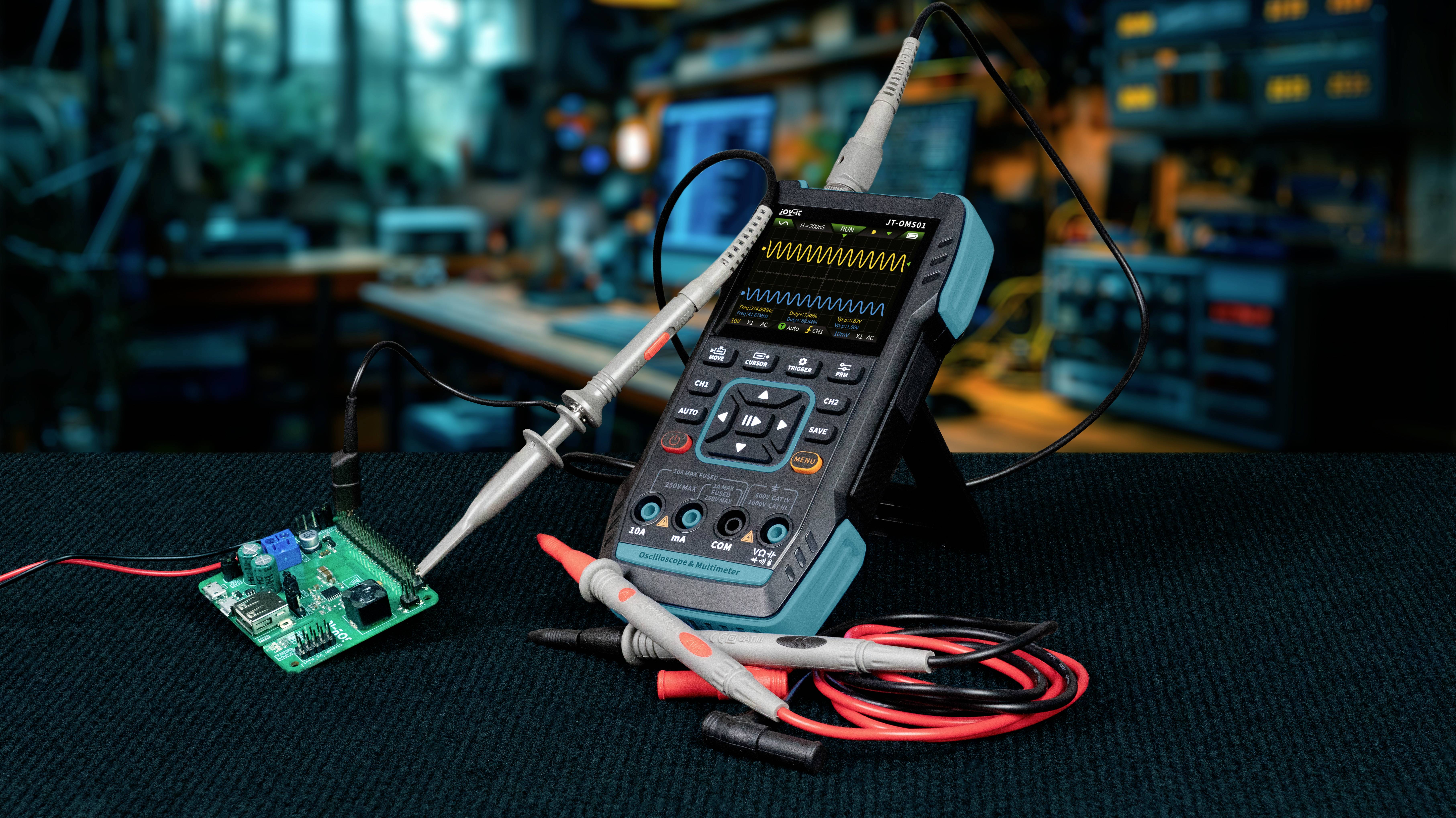 Oscyloskop leży na stole w warsztacie, podłączone do obwodu elektrycznego. W tle widoczne są narzędzia i urządzenia.