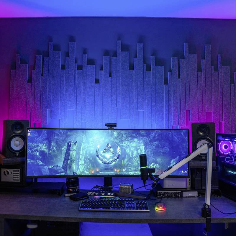 Stanowisko pracy z ultrapanoramicznym monitorem, otoczone głośnikami i oświetleniem RGB, prawdopodobnie przeznaczone do zastosowań multimedialnych.