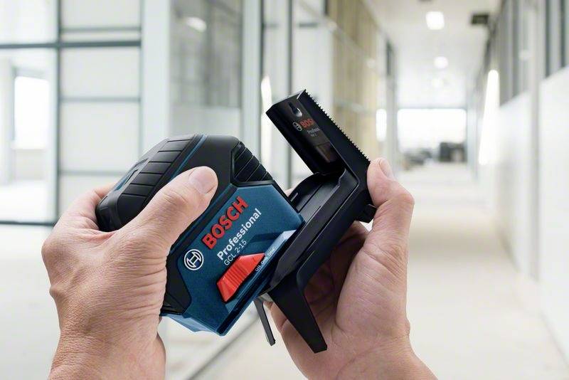 Dwie ręce trzymają laserowy przyrząd pomiarowy Bosch Professional w budynku biurowym, wskazując na precyzyjny pomiar w nowoczesnym otoczeniu.