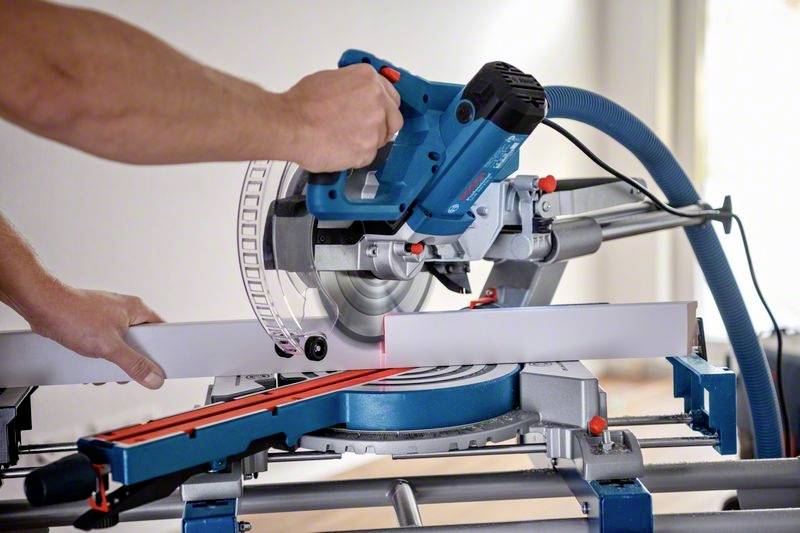 Osoba przecina biały profil aluminiowy niebieską piłą tarczową. Czerwona linia laserowa wskazuje linię cięcia.