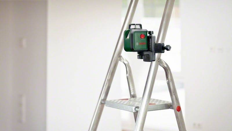 Drabina w pomieszczeniu z zielonym narzędziem laserowym przymocowanym z boku, służącym do wyrównywania obiektów lub wykonywania pomiarów.