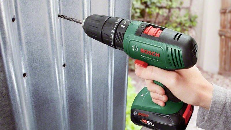Jedna ręka trzyma akumulatorowy wkrętak marki Bosch i wierci otwór w blasze metalowej. Otoczenie jest rozmyte.