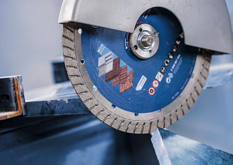 Tarcza diamentowa przecina kawałek metalu. Część tarczy jest zasłonięta osłoną ochronną.