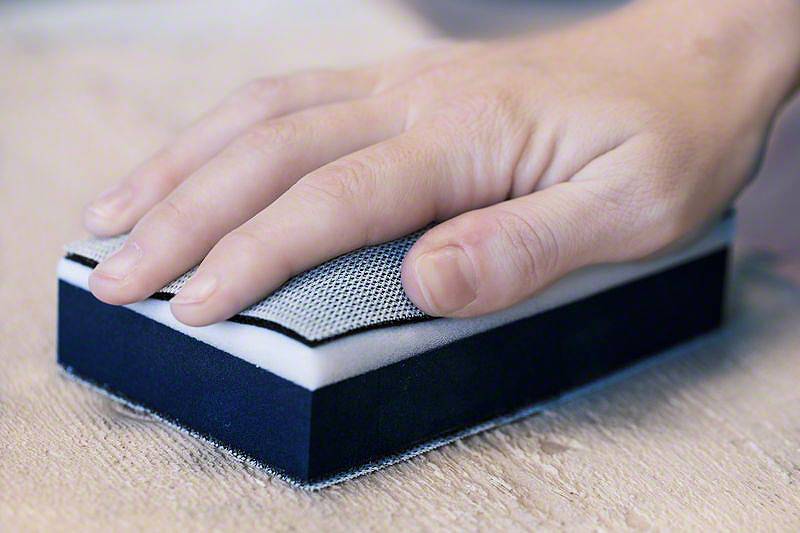 Dłoń prowadząca blok szlifierski po powierzchni drewna, aby ją wygładzić.