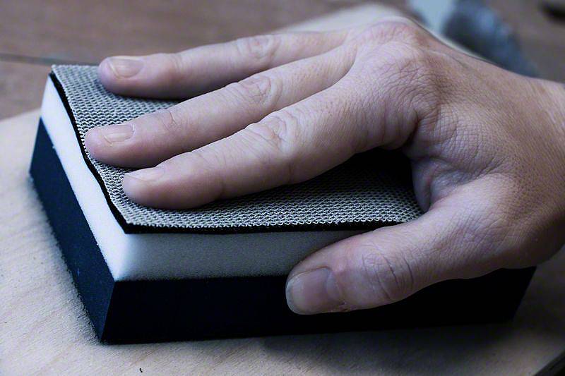 Dłoń trzyma blok szlifierski i szlifuje powierzchnię drewna.