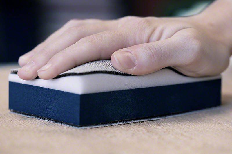 Ręka szlifuje drewnianą powierzchnię za pomocą bloku szlifierskiego.