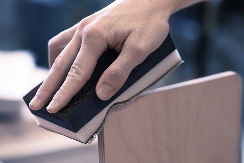 Jedna ręka szlifuje krawędź deski drewnianej za pomocą bloku szlifierskiego.