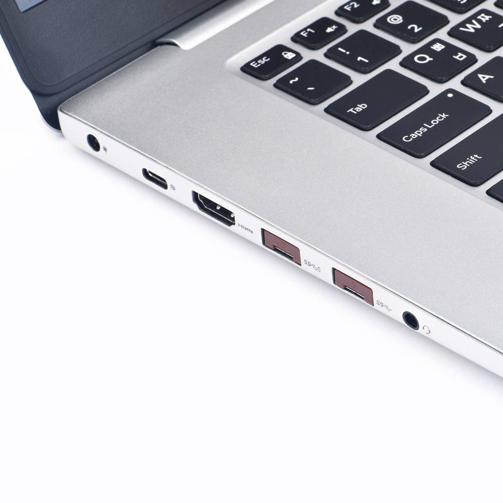 Srebrny laptop z otwartą klawiaturą na białym stole. Widoczne złącza: HDMI, porty USB oraz gniazdo słuchawkowe.