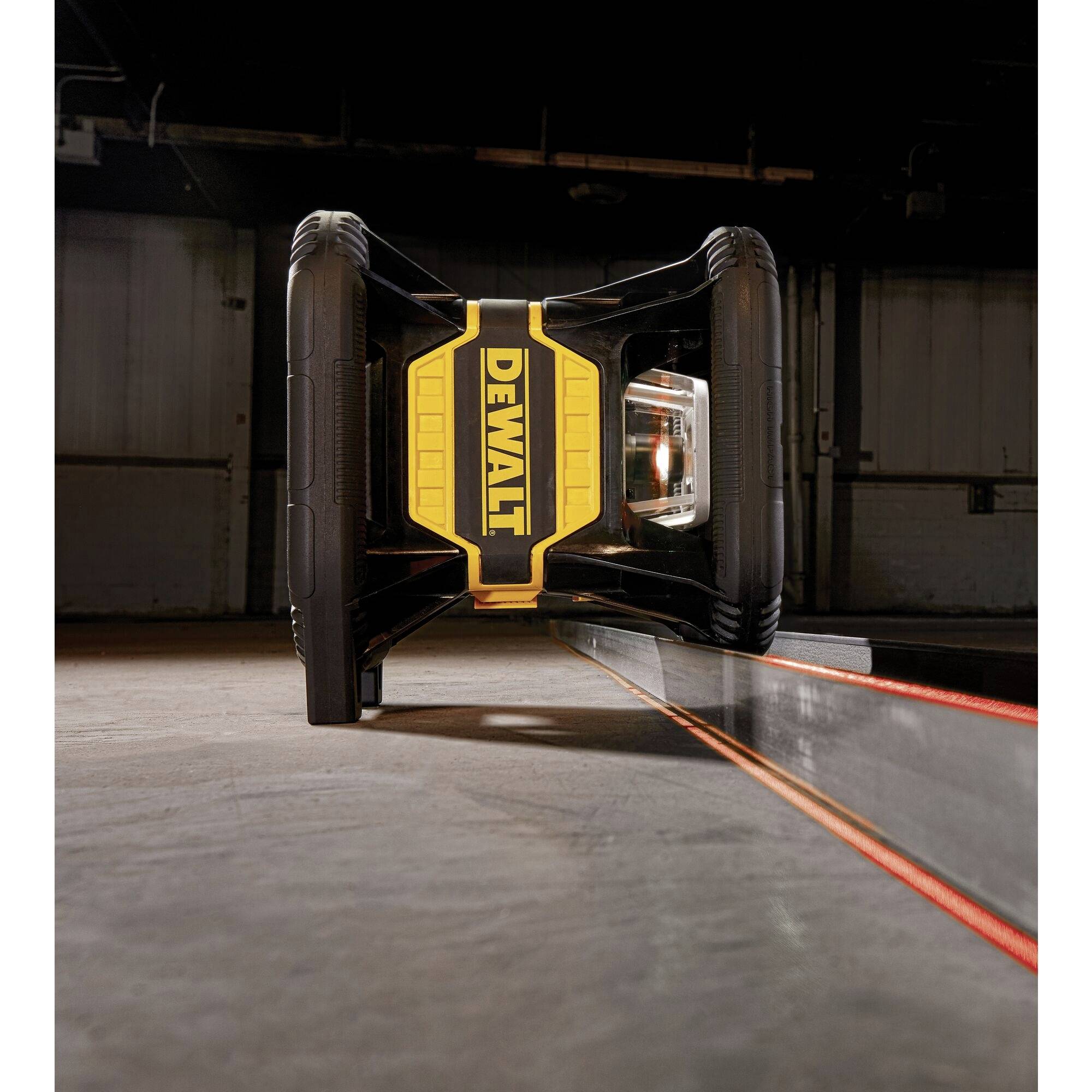 Żółty laserowy niwelator firmy DeWalt rzuca czerwoną linię na podłogę hali magazynowej. Służy do pomiarów budowlanych.