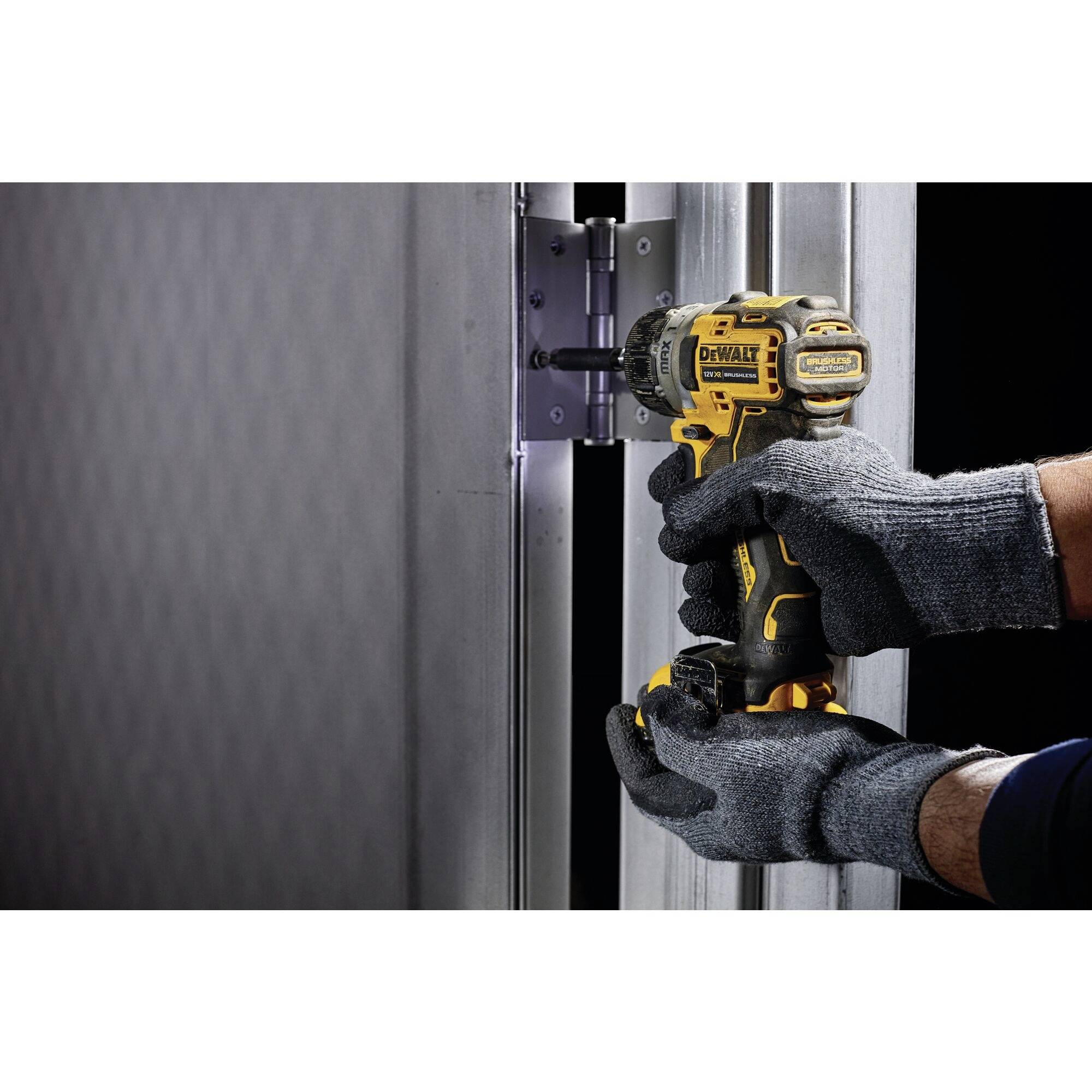 Osoba ubrana w rękawice robocze używa akumulatorowego wkrętaka do zamocowania zawiasu przy metalowych drzwiach.