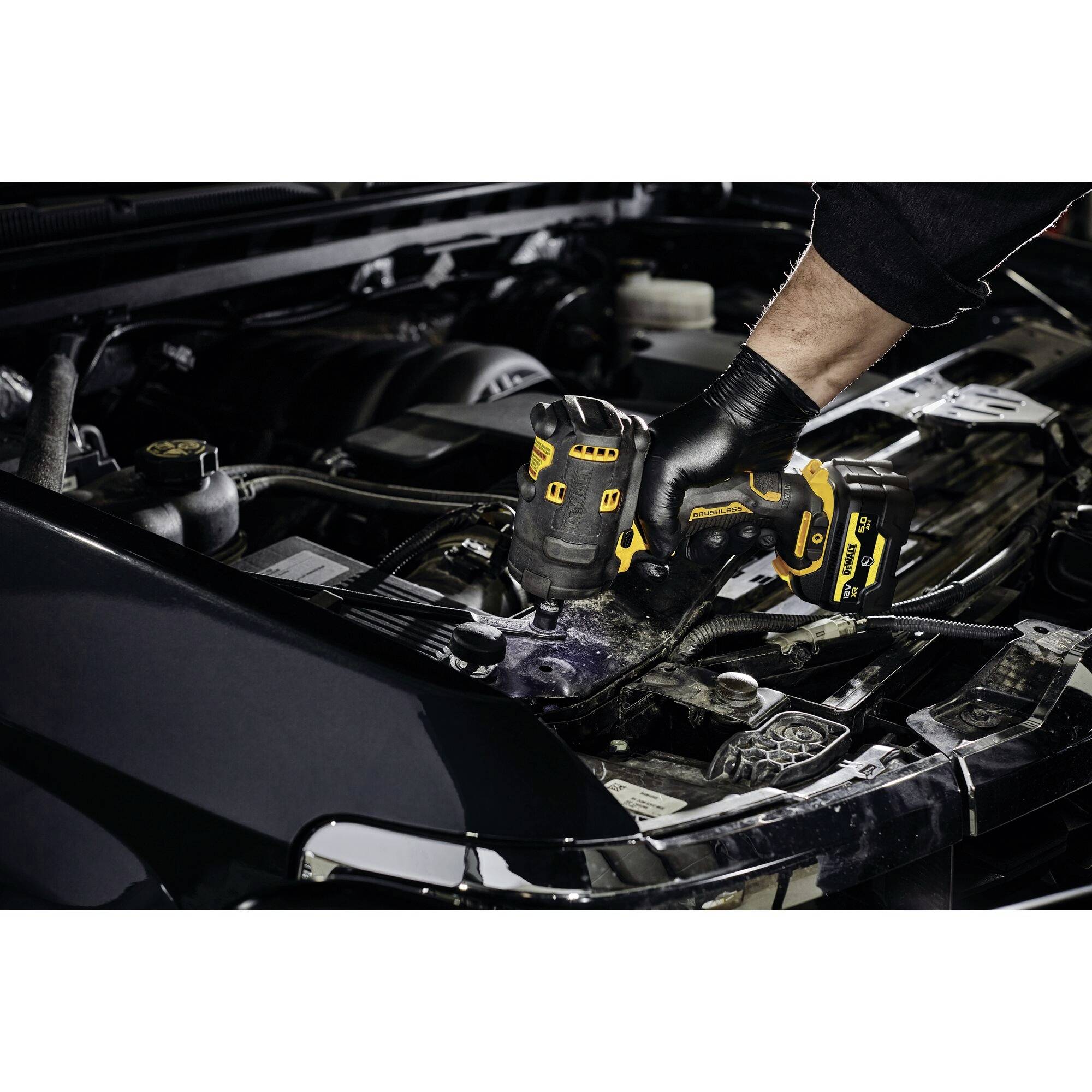 Osoba używa akumulatorowego wkrętarki podczas pracy w otwartej przestrzeni silnika samochodu. Ręka jest zabezpieczona rękawicą.