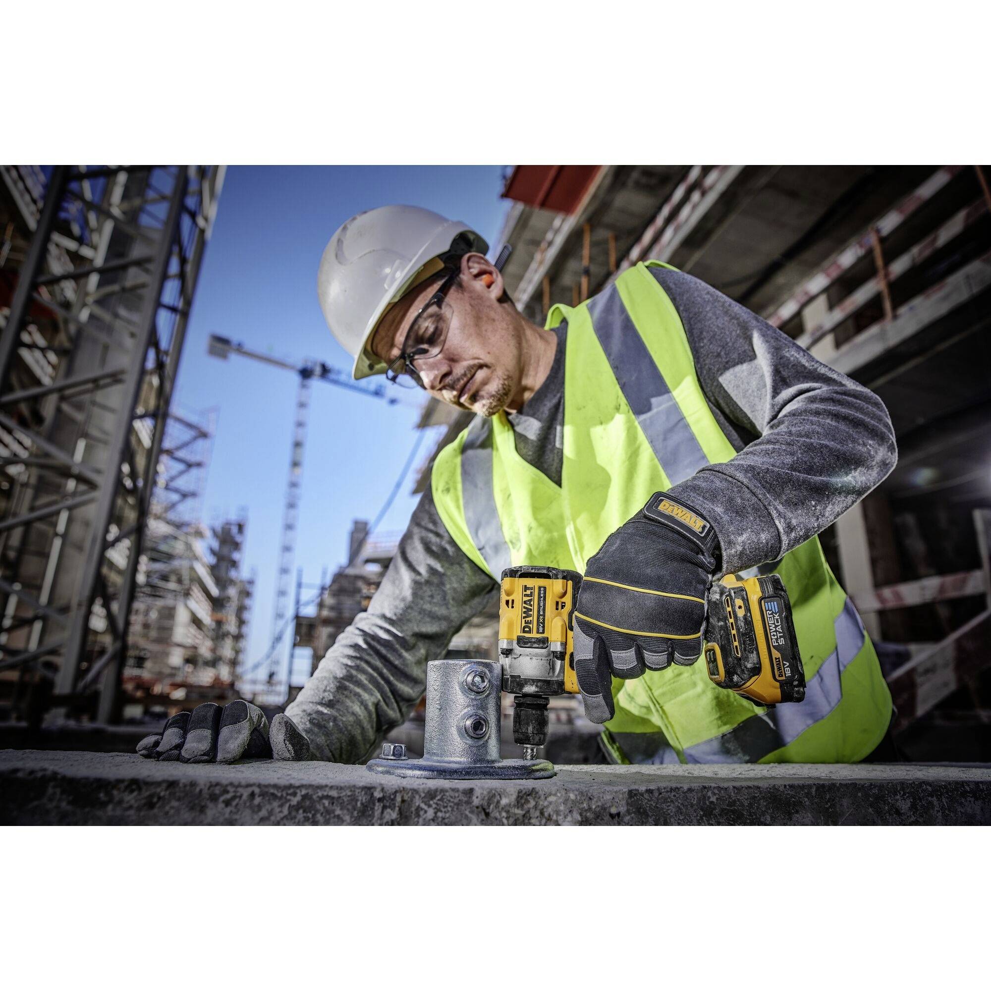 Robotnik budowlany w odzieży ochronnej używa wiertarki, aby zamocować blachę metalową na placu budowy. W tle widać rusztowania.