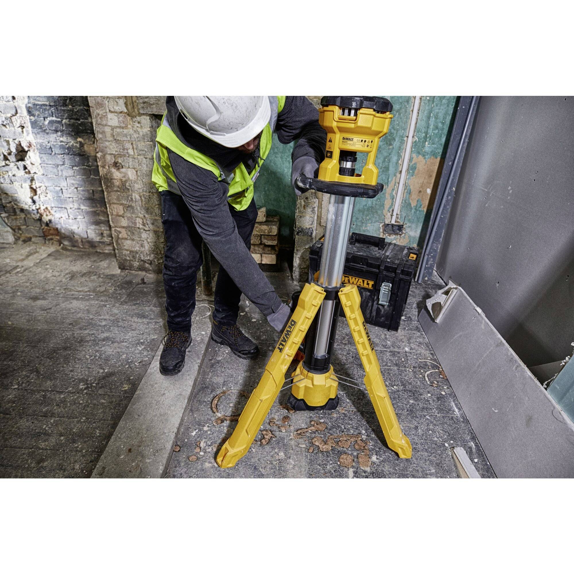 Osoba ustawia żółty statyw budowlany na placu budowy. W tle widać ściany i narzędzia budowlane.