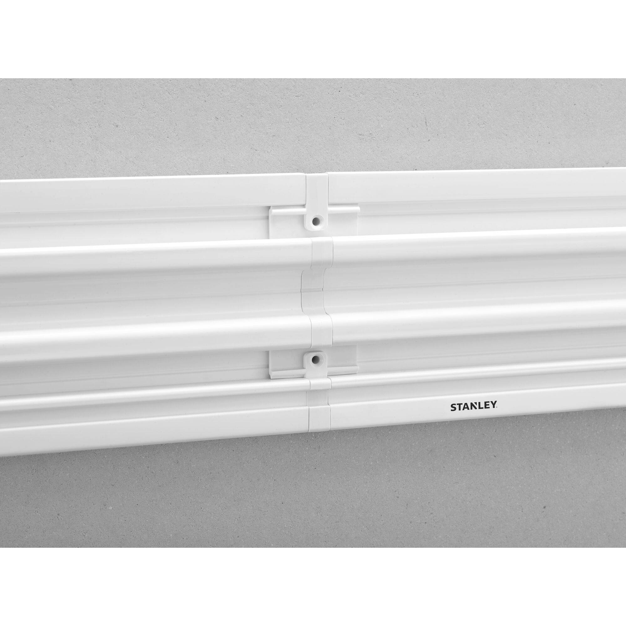 Biała plastikowa szyna z nadrukiem 'STANLEY', zamontowana na szarej ścianie.