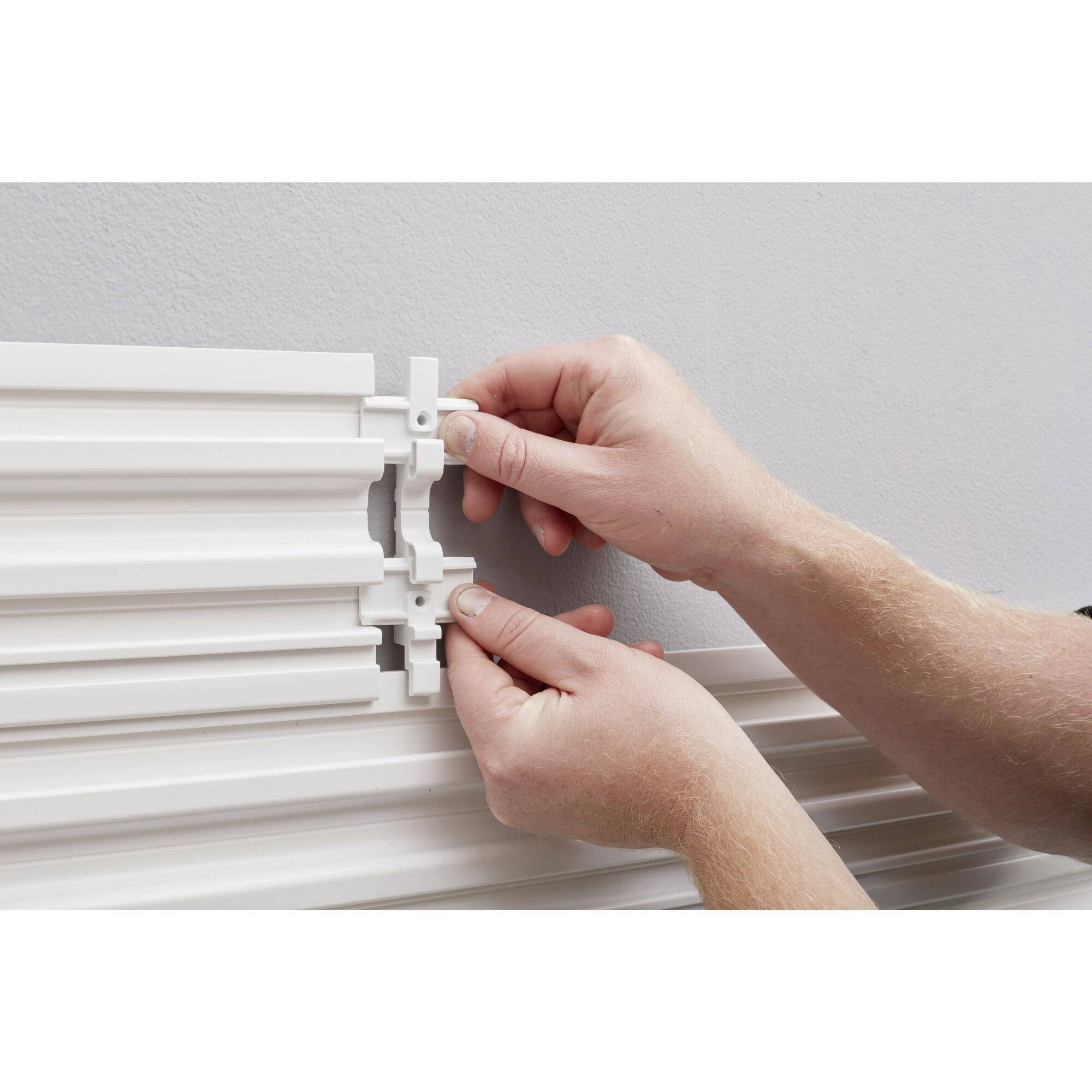 Dwie ręce montują białą listwę prowadnicową z tworzywa sztucznego na ścianie. Osoba mocuje małą złączkę do szyny.