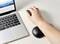 Osoba pracuje na laptopie z ergonomiczną podkładką pod nadgarstek i trzyma mysz. Na ekranie laptopa wyświetlane są grafiki.