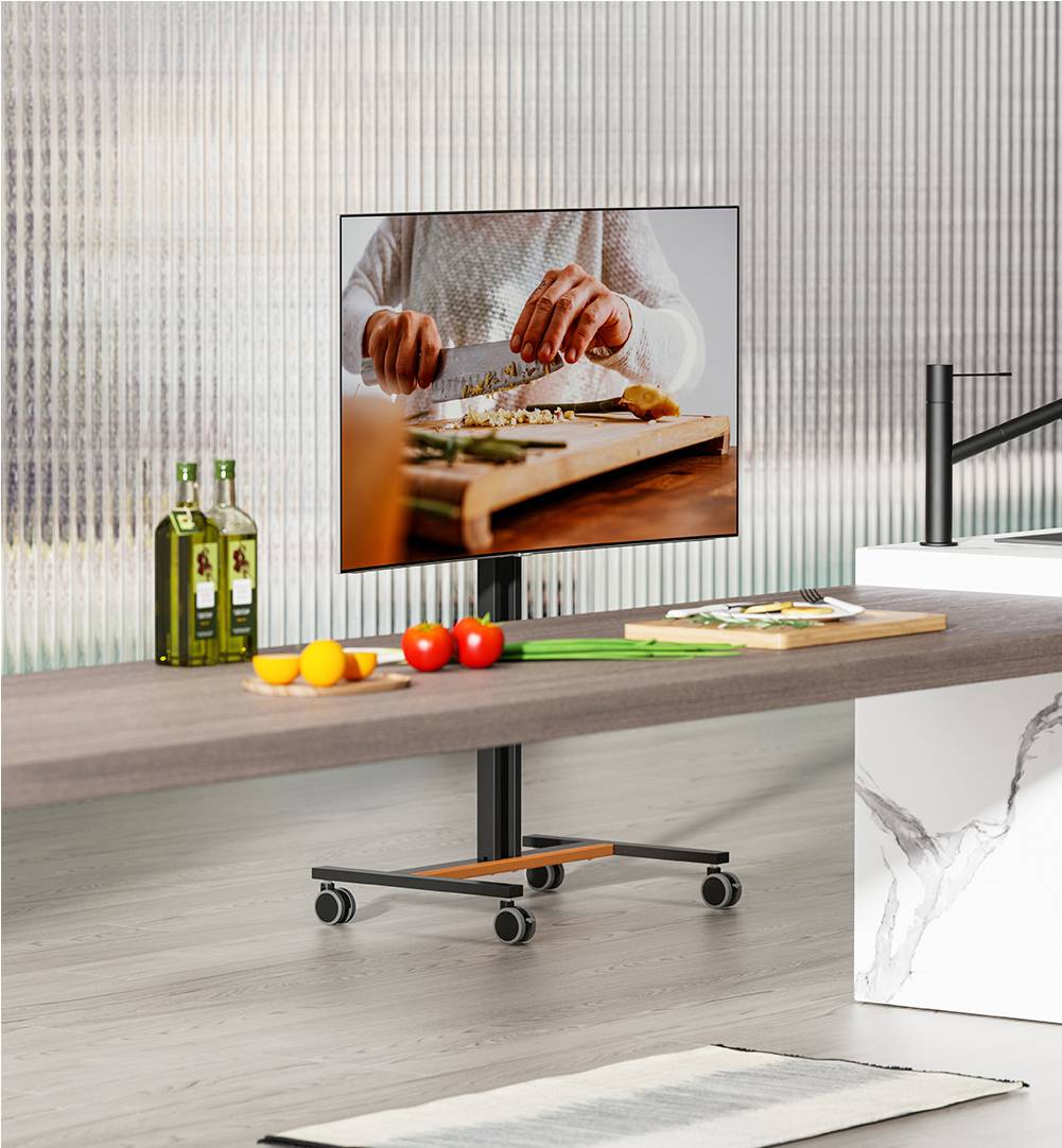 Telewizor wyświetla zbliżenie rąk krojących warzywa. Na pierwszym planie stoją butelki i świeże warzywa na stole.