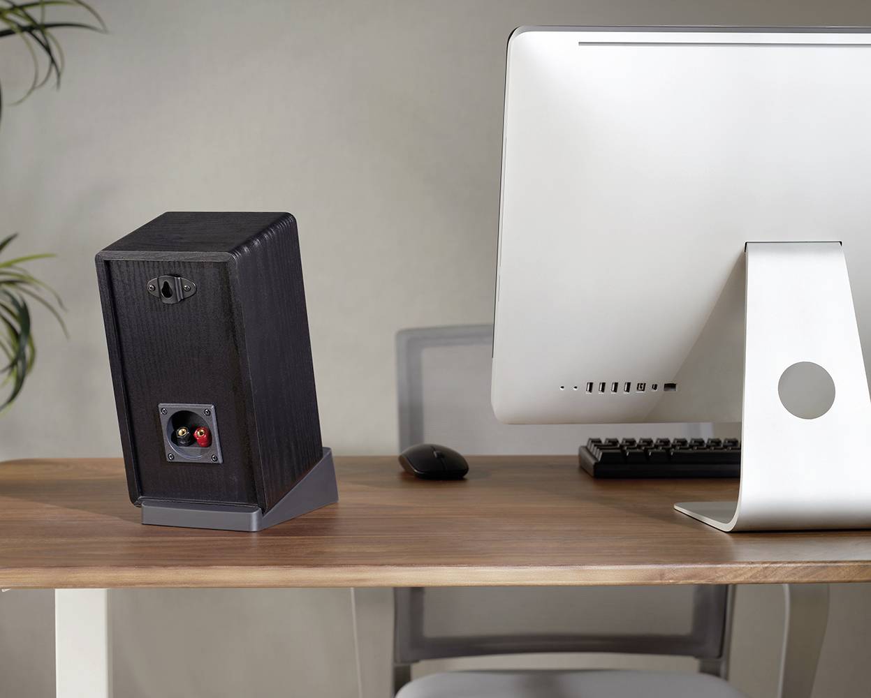 Biurko z monitorem komputerowym, klawiaturą, myszą i głośnikiem w tle.