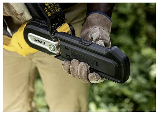 Osoba w rękawicach trzyma piłę łańcuchową jedną ręką, skupiając się na uchwycie i obszarze ostrza. Tło stanowi rozmyte zielone listowie.