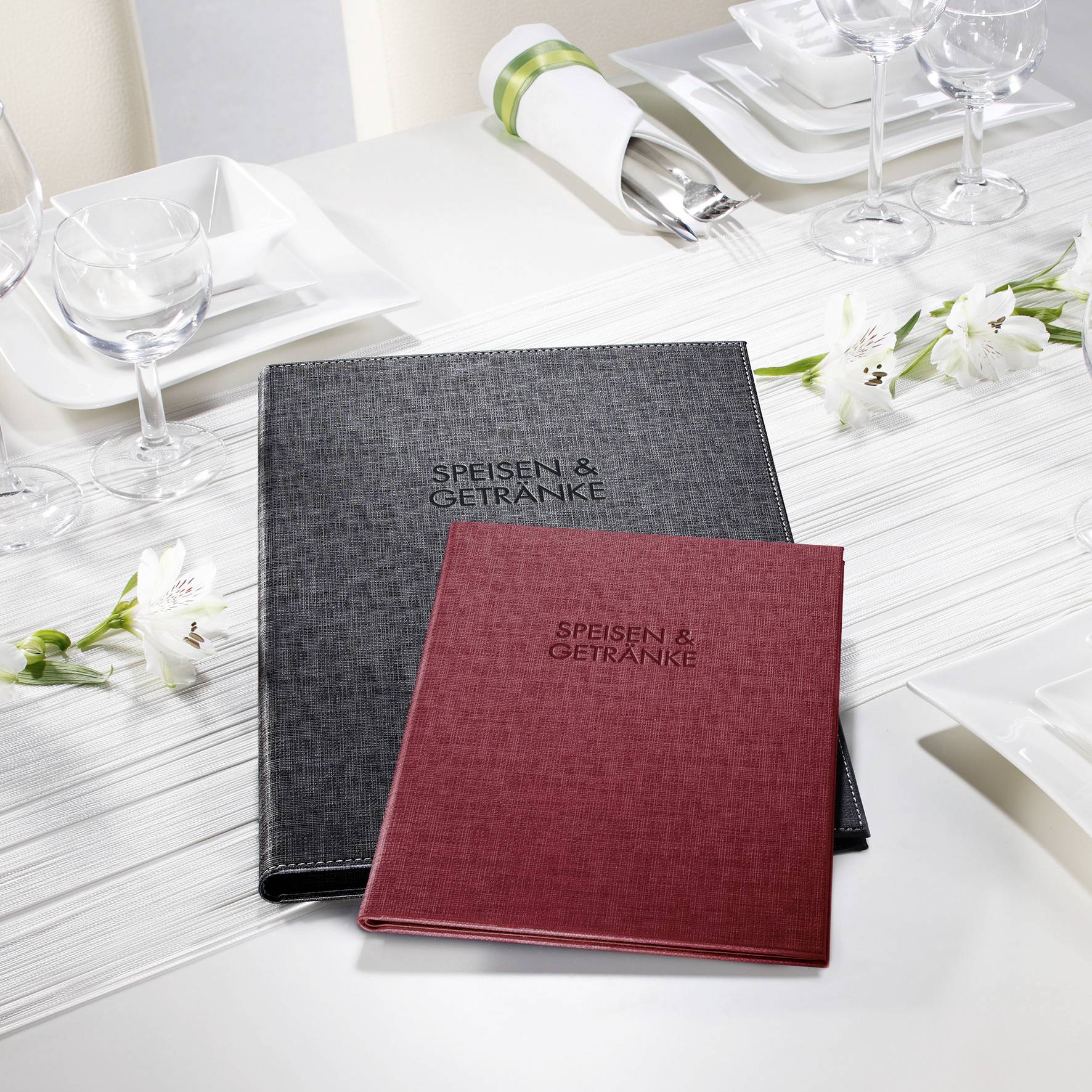 Biała dekoracja stołu z kwiatami, kieliszkami oraz kartami menu w kolorach czarnym i czerwonym z napisem 'Dania i napoje'.