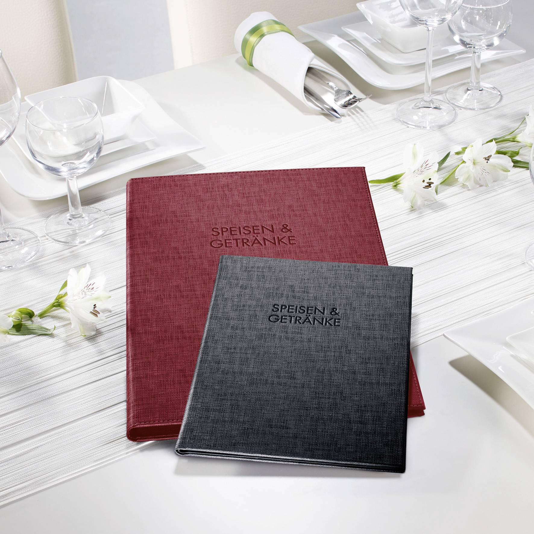 Na stole z białymi orchideami i zastawą stołową leżą dwie karty menu. Widoczna jest większa czerwona karta i mniejsza czarna karta.