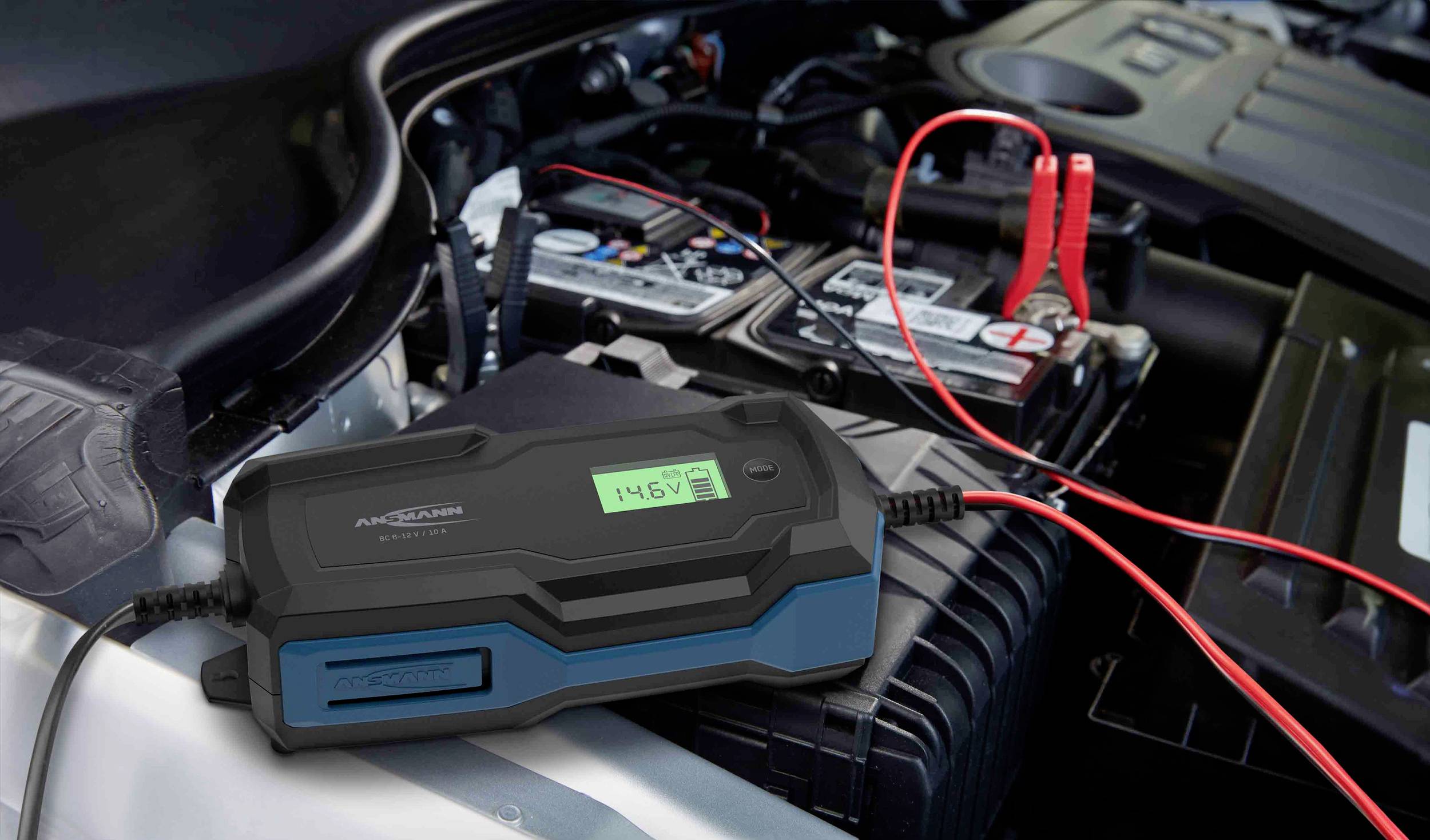 Samochód z otwartą maską prezentuje ładowarkę akumulatora podłączoną do akumulatora samochodowego. Wyświetlacz wskazuje '14,6V'.