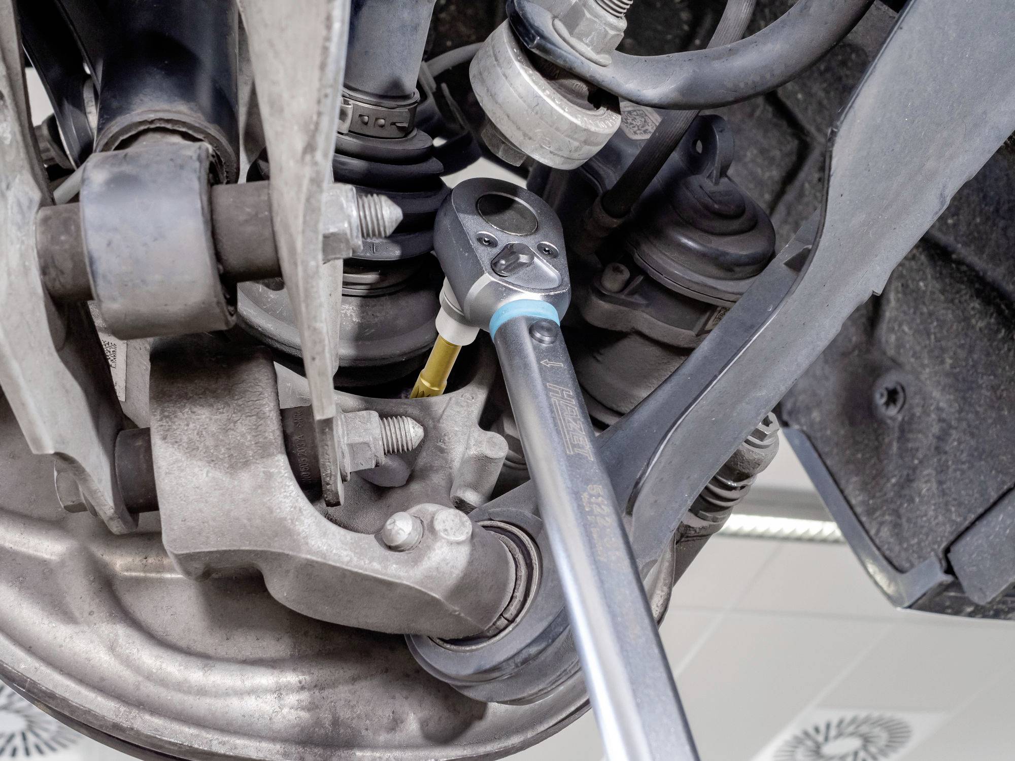 Mechanik naprawia element zawieszenia samochodu kluczem w warsztacie samochodowym.