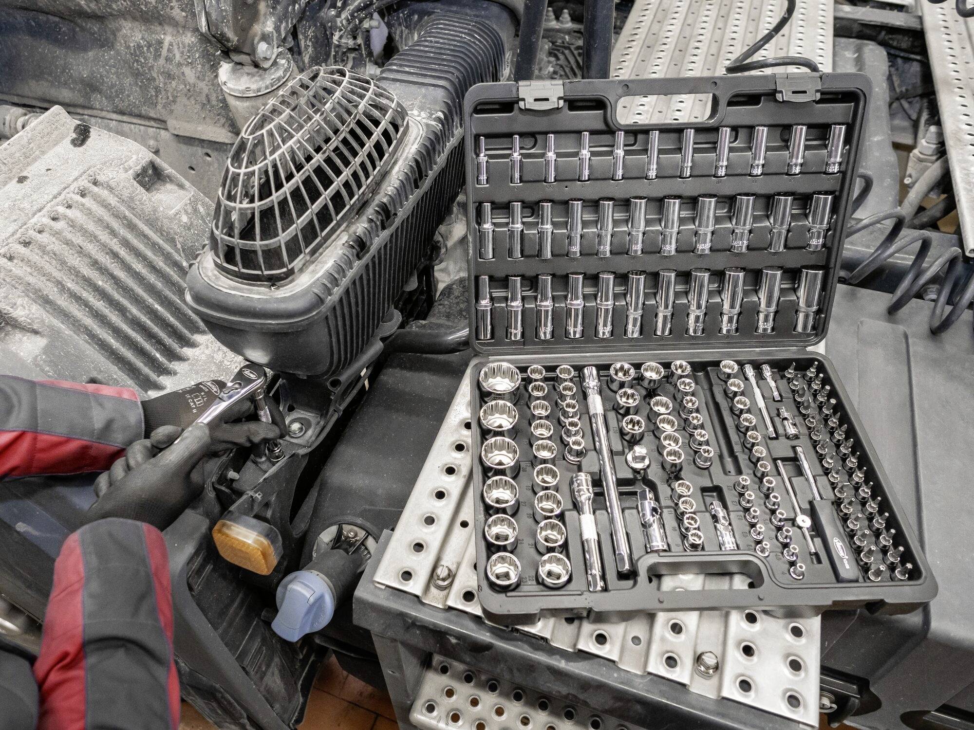 Mechanik pracuje z grzechotką obok otwartego zestawu kluczy nasadowych w walizce na stole warsztatowym.