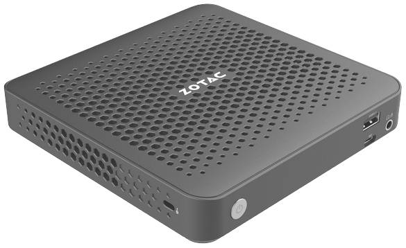 Kompaktowy, szary mini-PC z otworami wentylacyjnymi i gniazdem USB z boku. Na górze widoczne jest logo marki 'ZOTAC'.