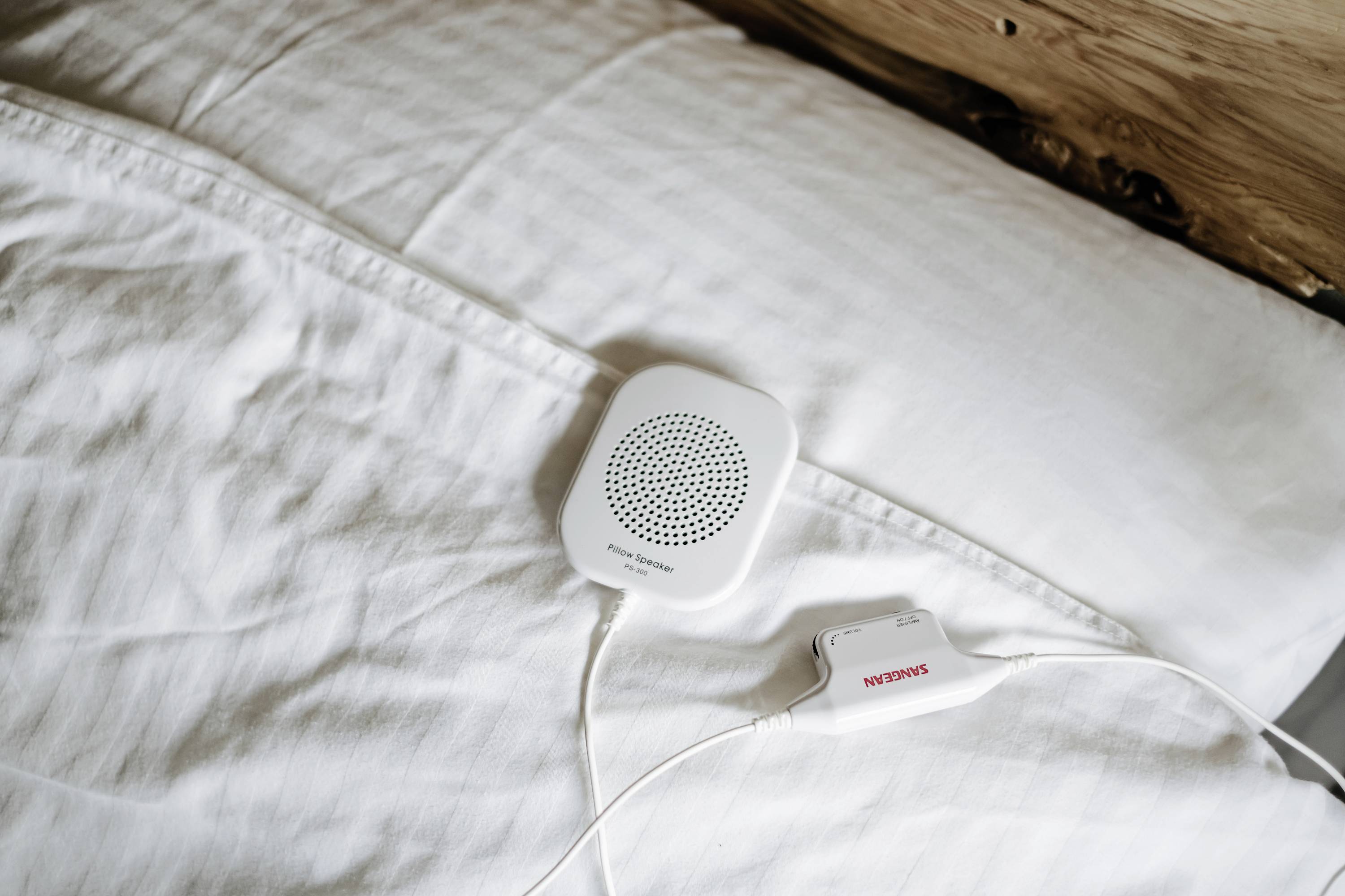 Mały biały gadżet głośnikowy leży na białej poduszce, podłączony do nośnika pamięci.