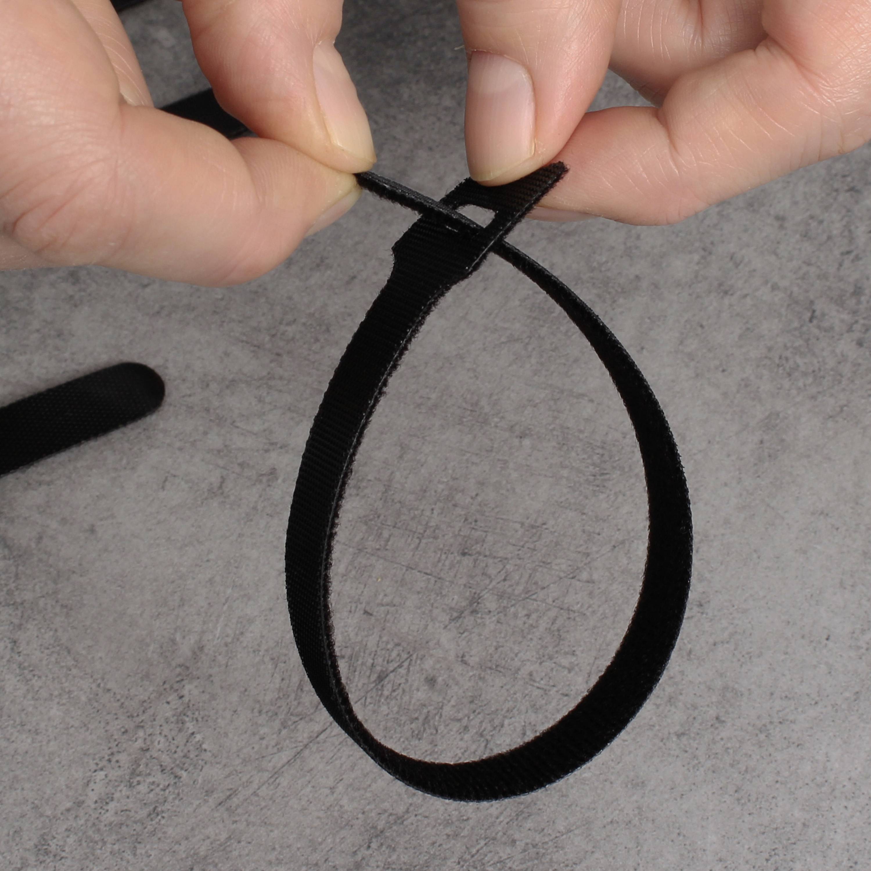 Dwie ręce zaciskają czarny kabel zaciskowy na szarym podłożu.