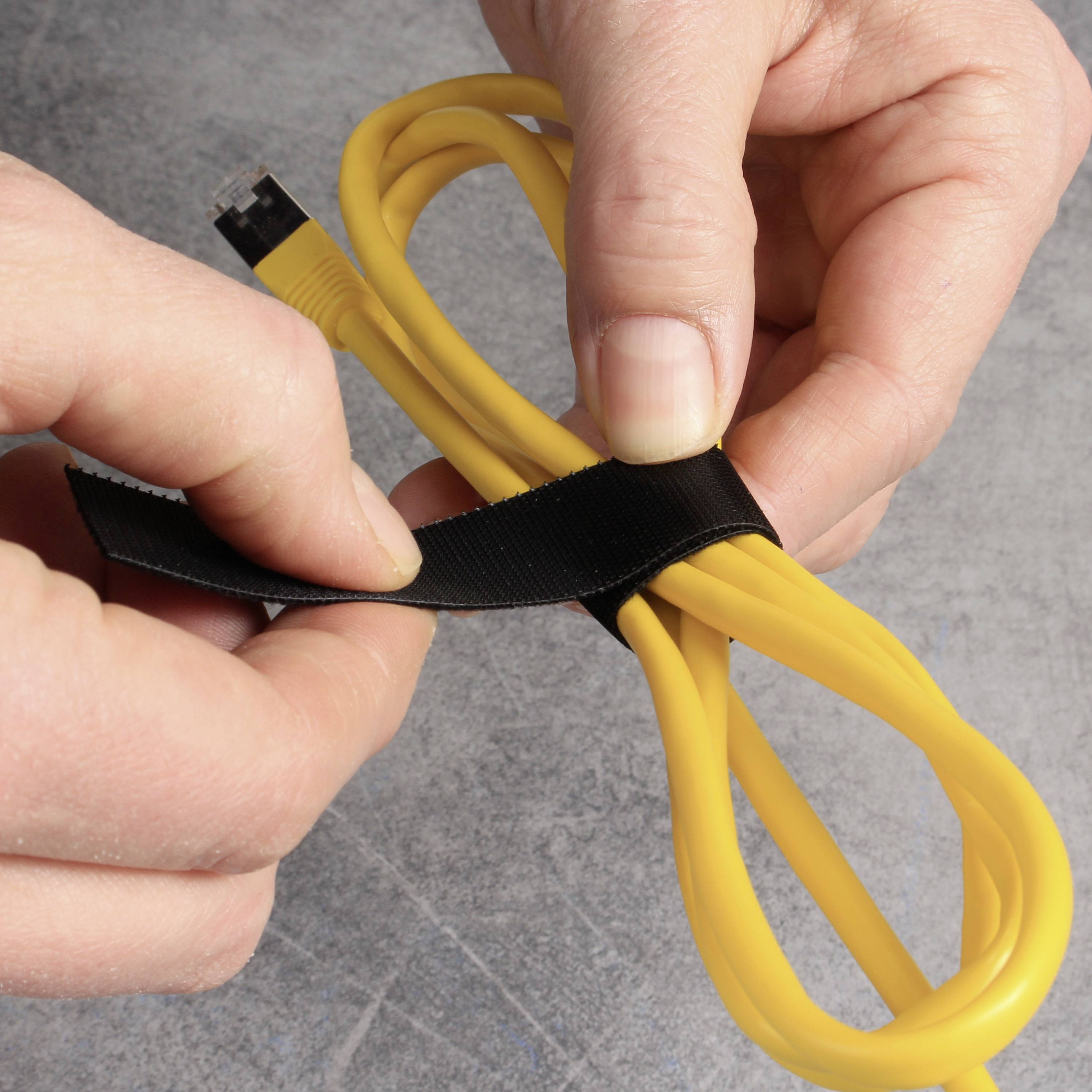 Dwie ręce mocują żółty kabel sieciowy czarną taśmą klejącą.