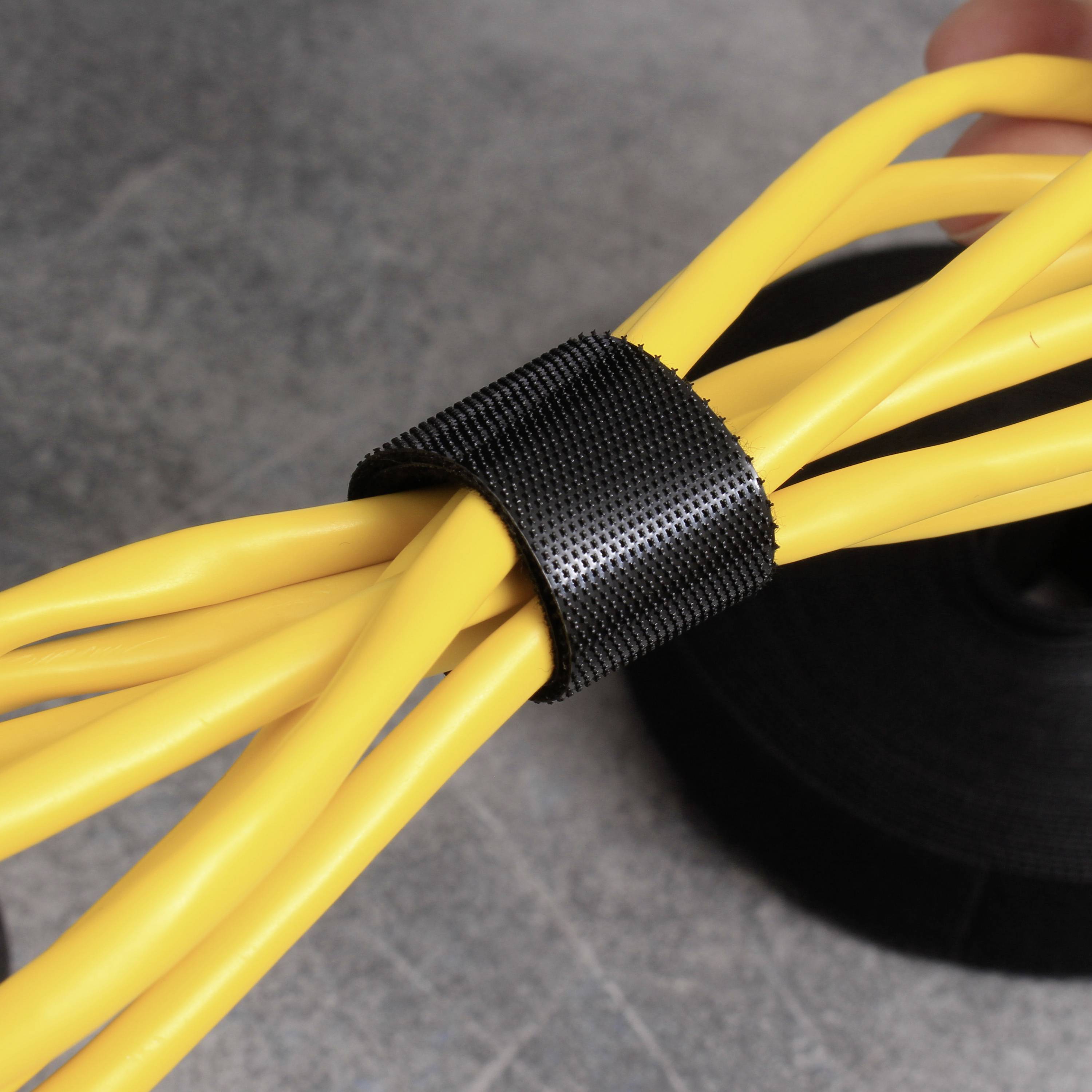 Pęk żółtych kabli jest związany czarną opaską rzepową. Na tle widać rolkę taśmy rzepowej.