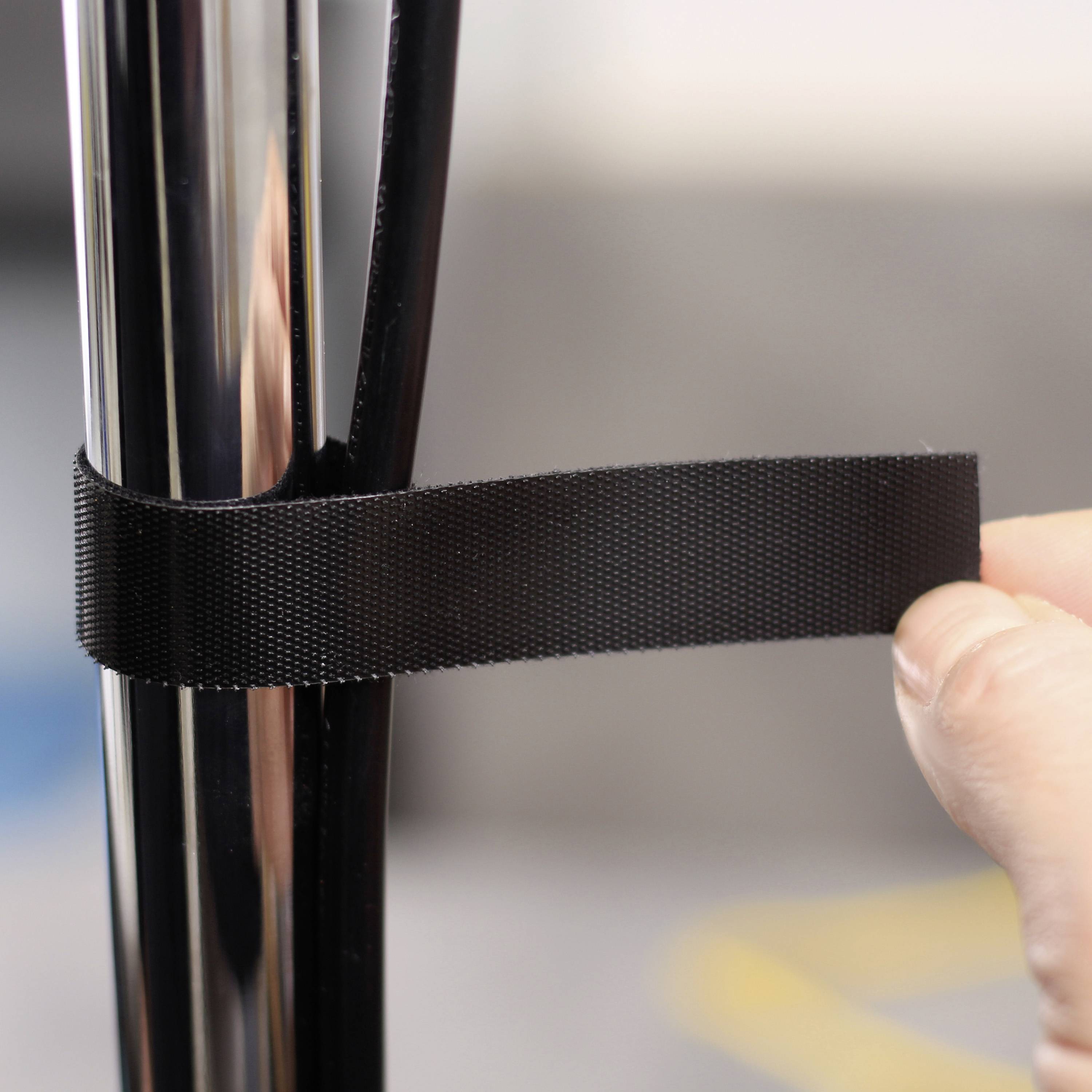 Jedna ręka mocuje czarną opaskę rzepową wokół srebrnej metalowej rurki.