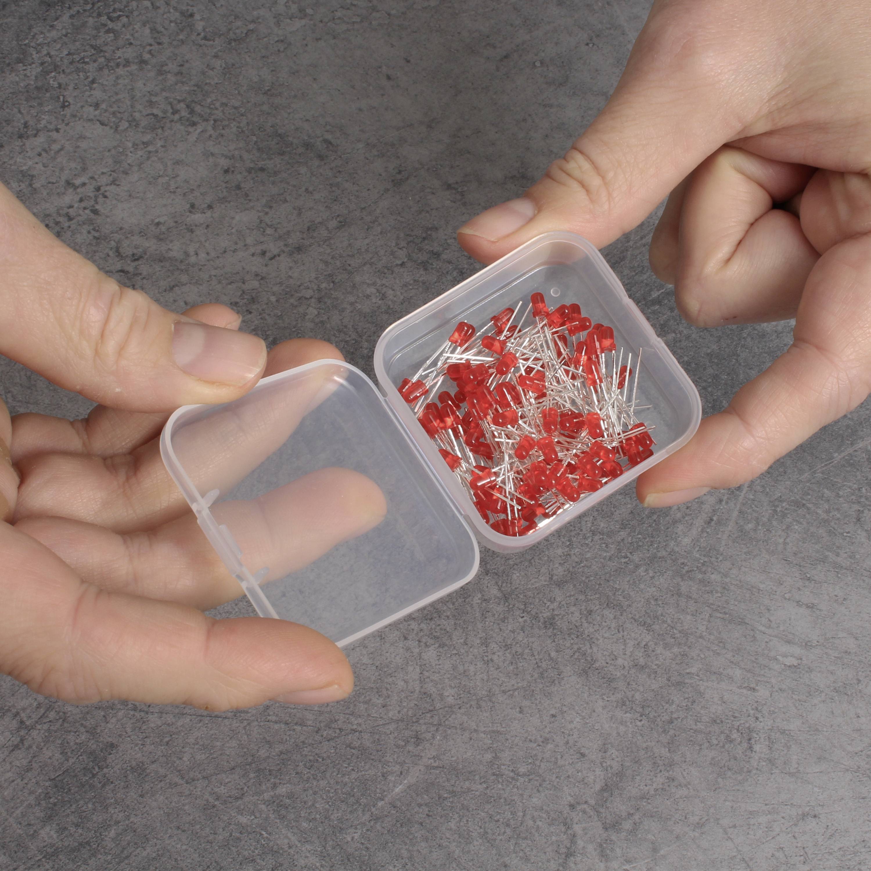 Dwie ręce trzymają otwarte plastikowe pudełko z licznymi czerwonymi diodami LED na szarym podłożu.