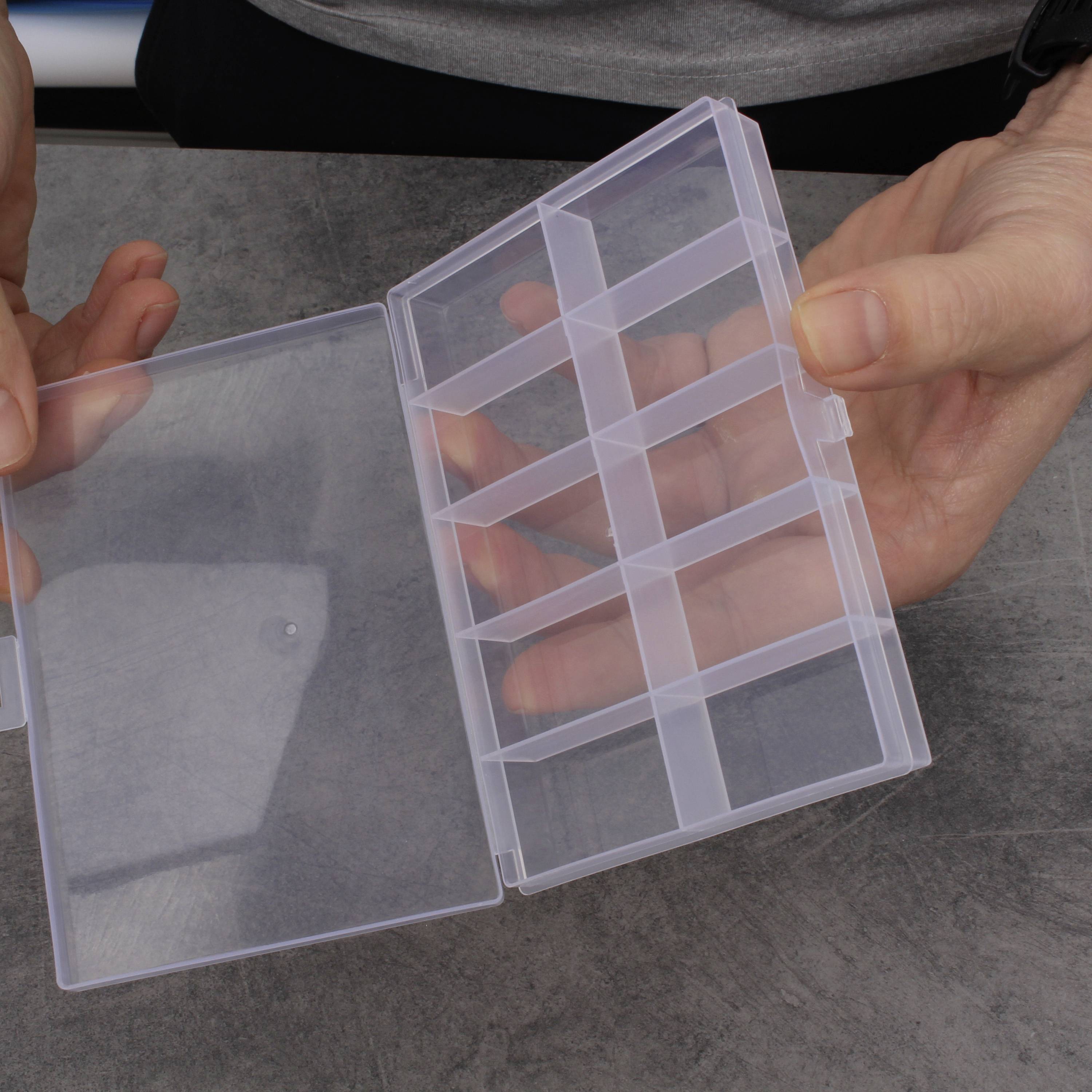 Osoba otwiera pusty, przezroczysty organizer z tworzywa sztucznego z wieloma przegródkami na stole.