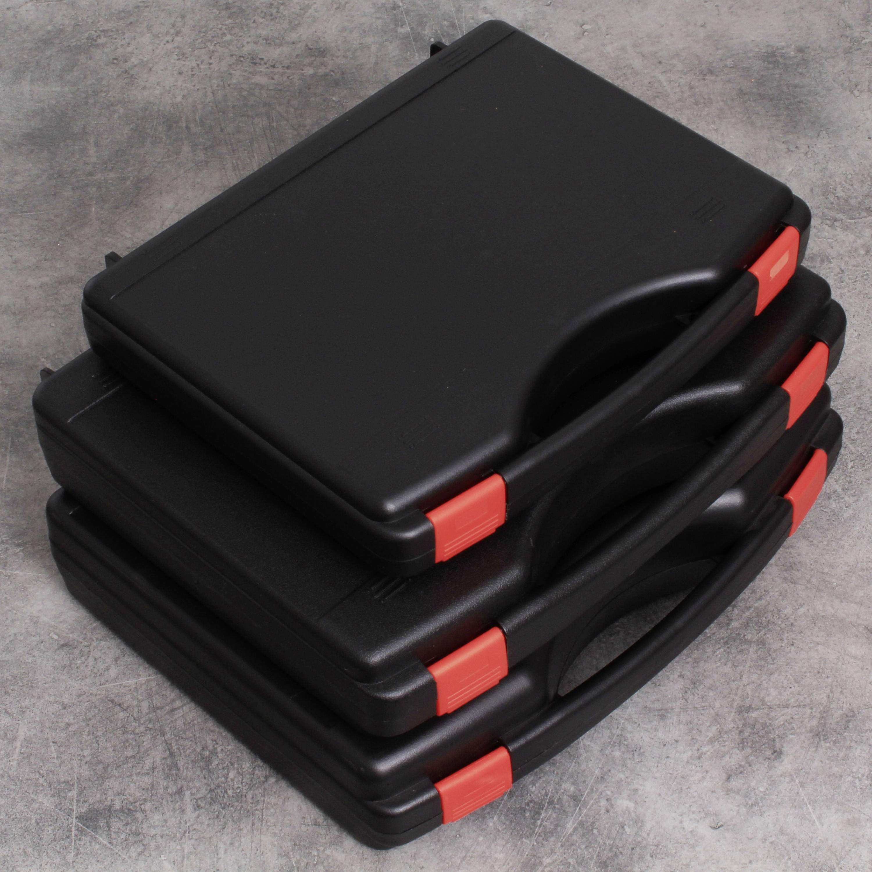 Trzy czarne walizki ułożone jedna na drugiej z czerwonymi zamkami, leżące na szarej powierzchni.