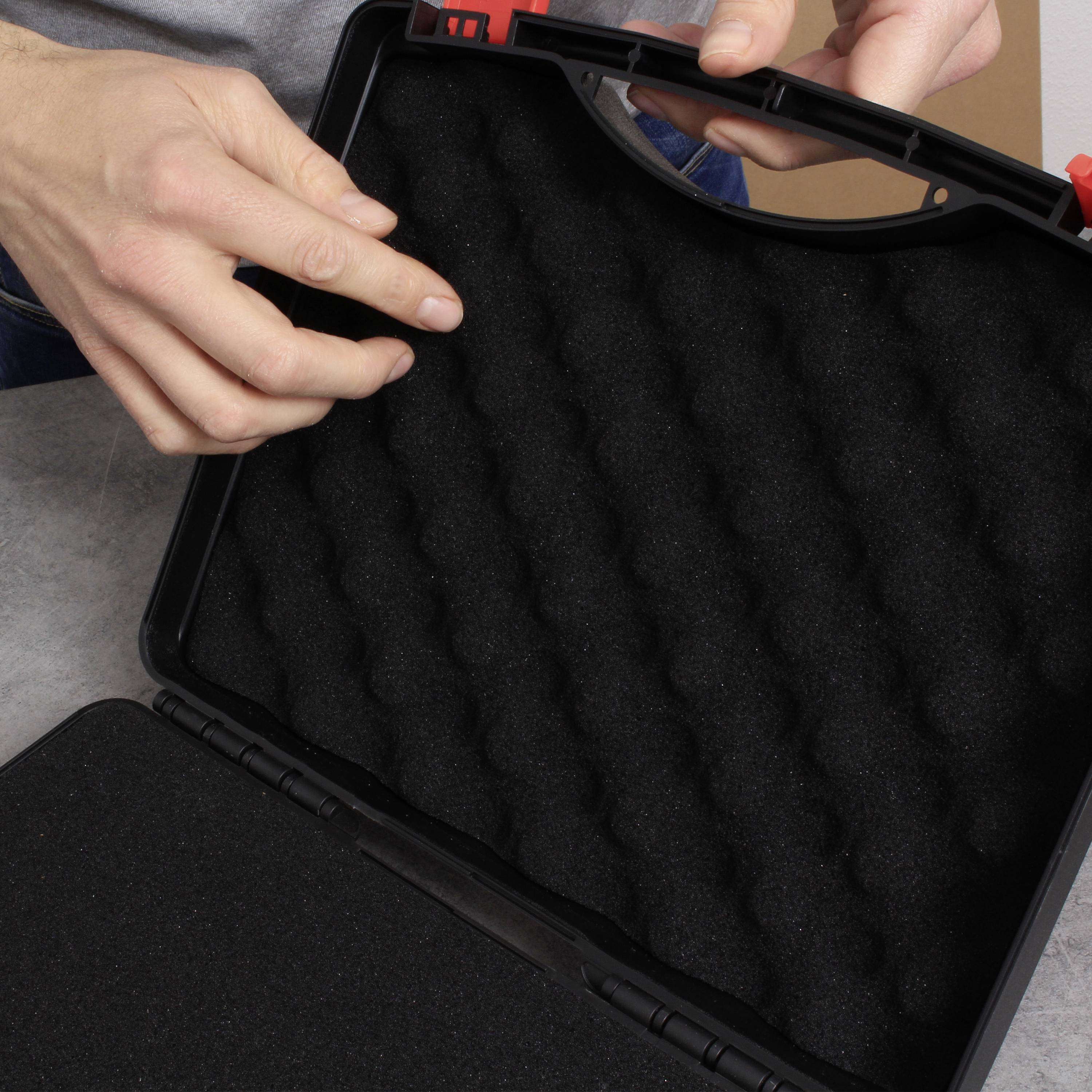 Dwie ręce otwierają czarną walizkę z wyłożonym wyścieleniem wewnątrz.