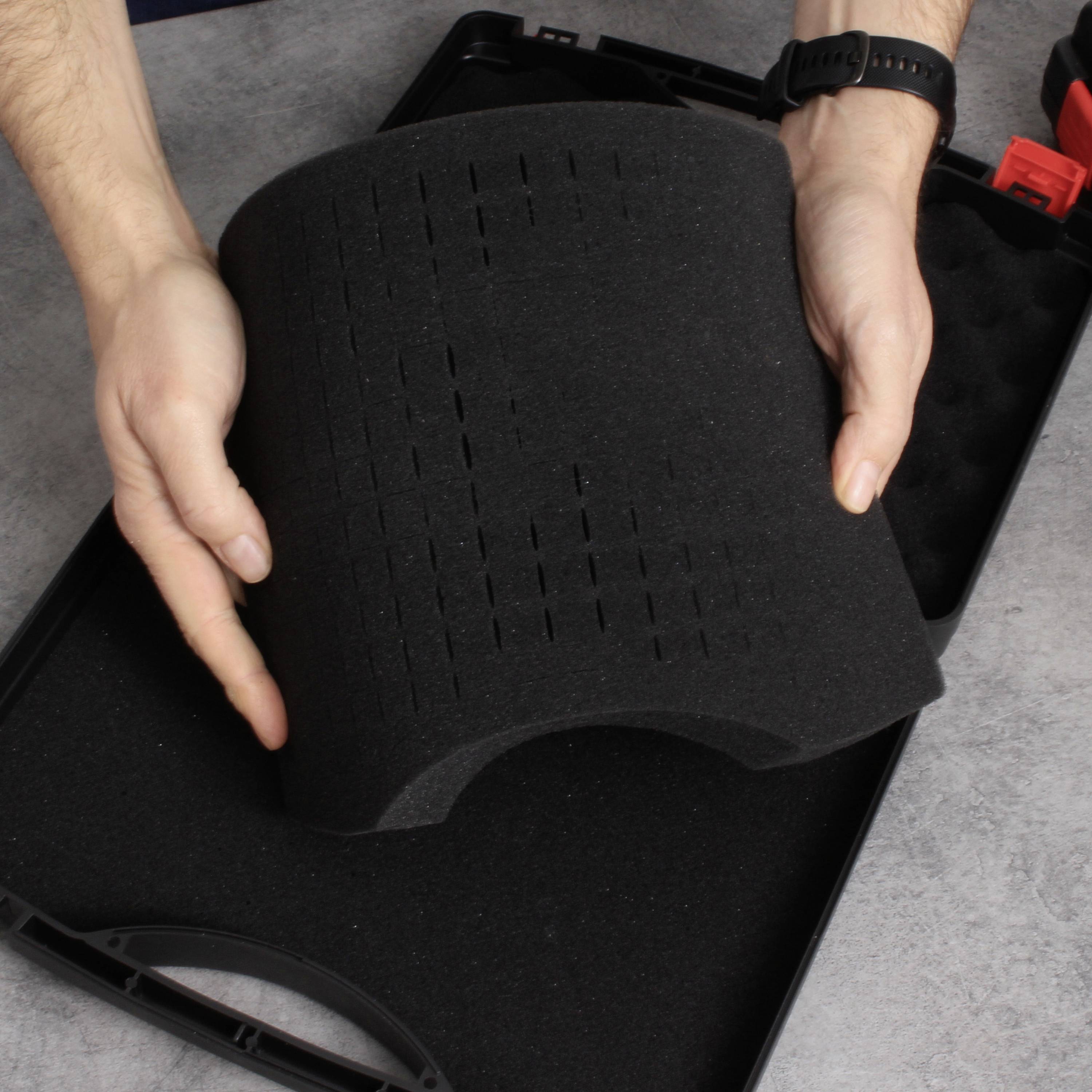 Osoba wyjmuje czarny, wyściełany element z pianki z walizki o dokładnie dopasowanym kształcie, prawdopodobnie przeznaczonej do ochrony delikatnych urządzeń.