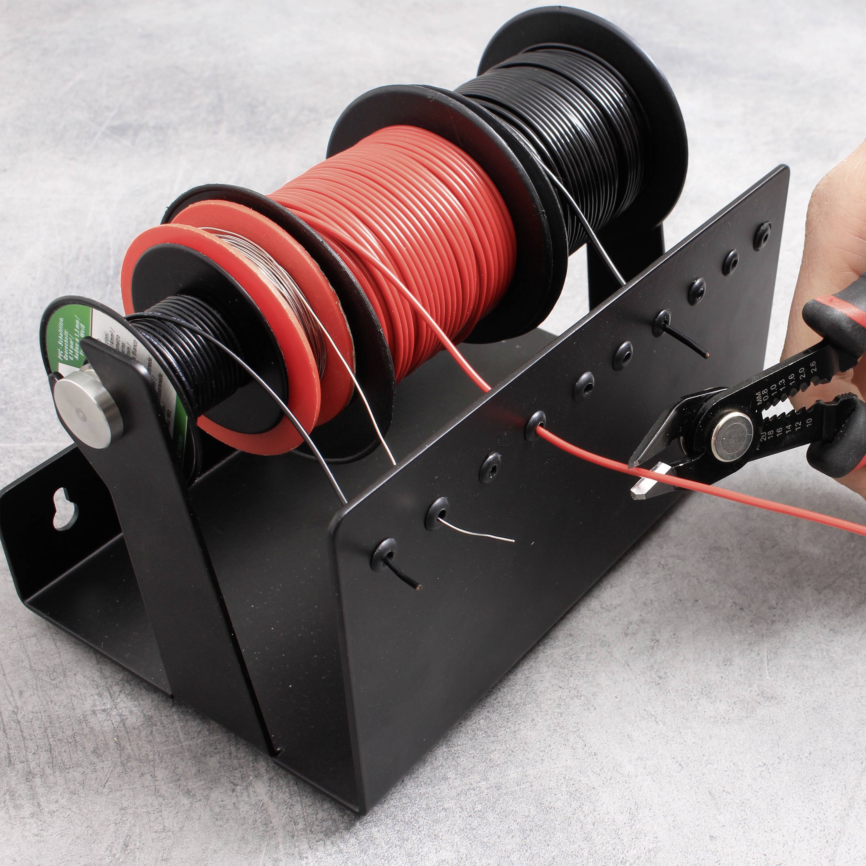 Szpula z czerwonymi i czarnymi przewodami na uchwycie. Dłoń wyciąga czerwony przewód. Środowisko pracy z szarym tłem.