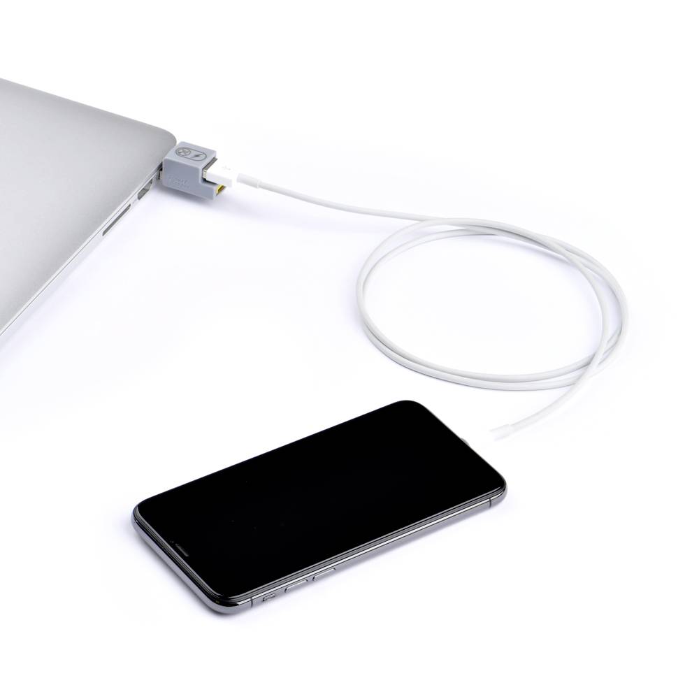 Smartfon leży obok laptopa, podłączony do niego kablem ładującym.