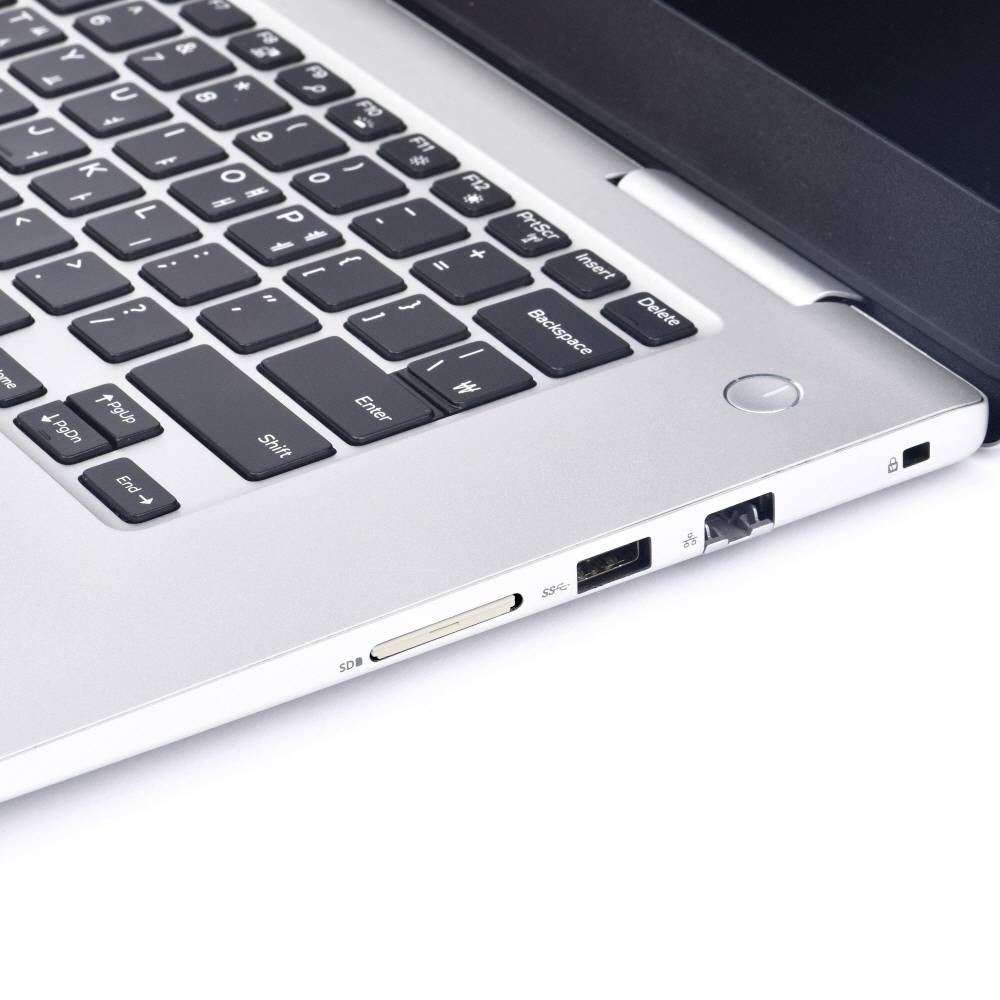 Srebrny laptop z klawiaturą, złączem USB i slotem na kartę SD na białym tle. Urządzenie jest częściowo otwarte.
