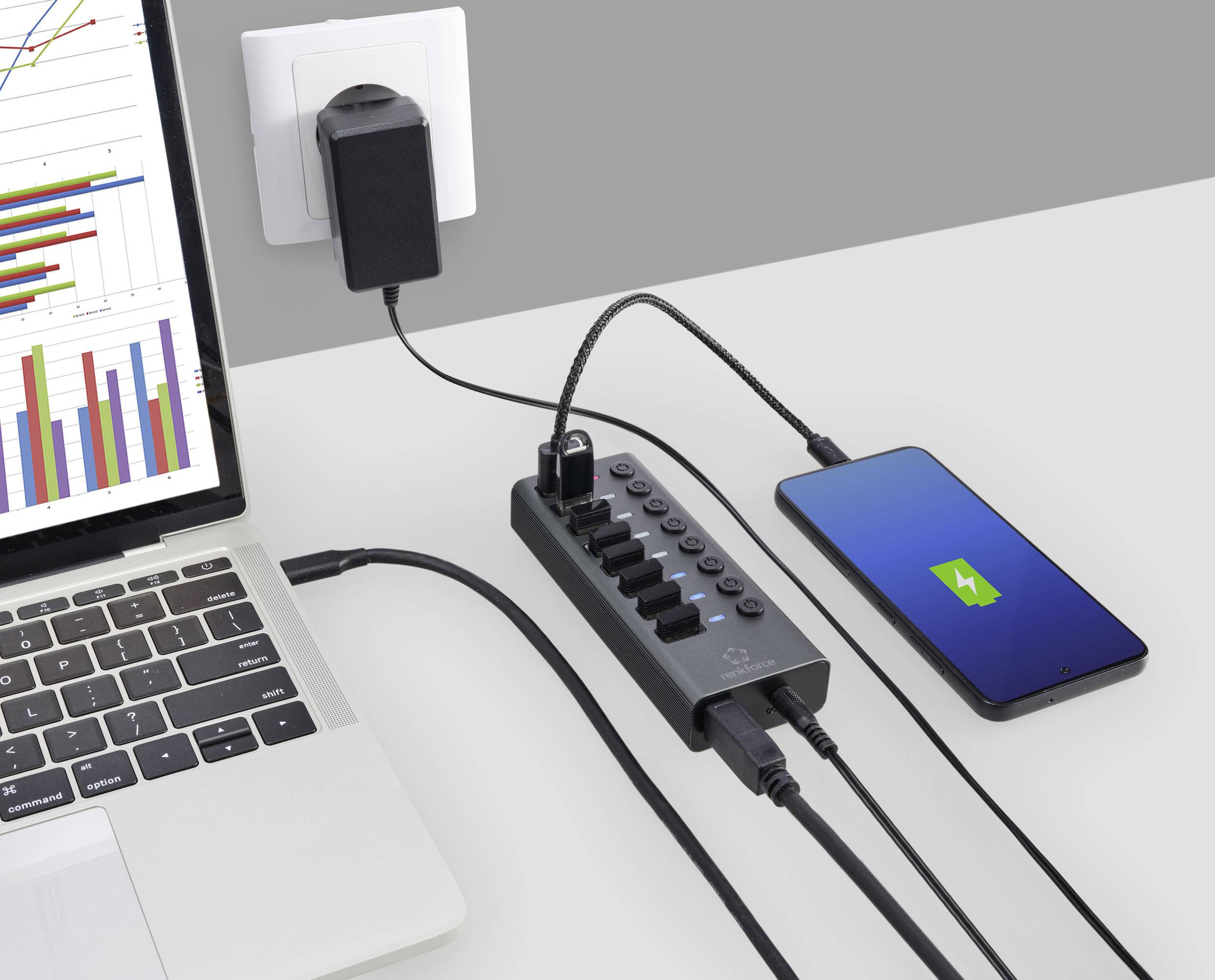 Smartfon i laptop są podłączone do listwy zasilającej, która jest włączona do gniazdka ściennego. Telefon wyświetla symbol ładowania.