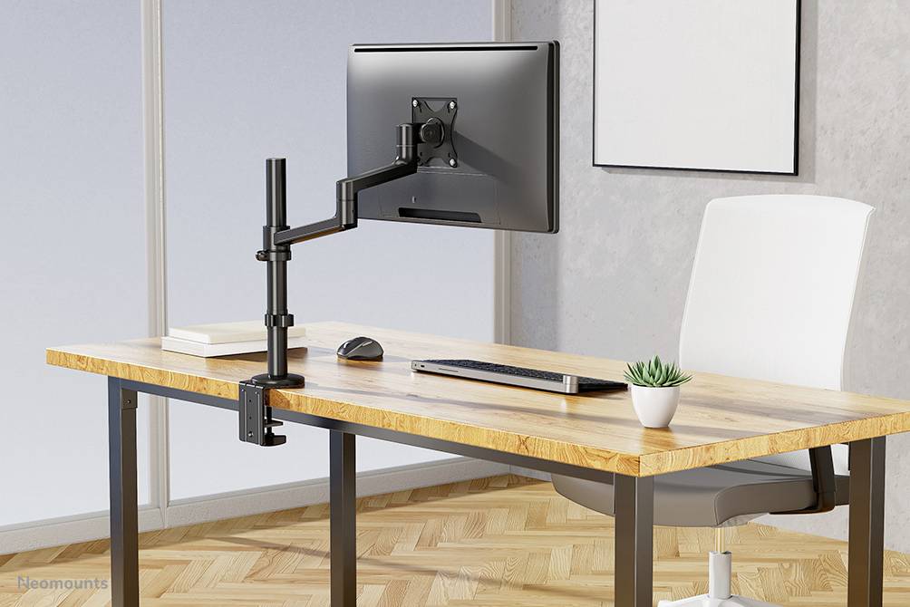 Biurko z monitorem na regulowanym ramieniu, klawiaturą, myszą i małą rośliną.