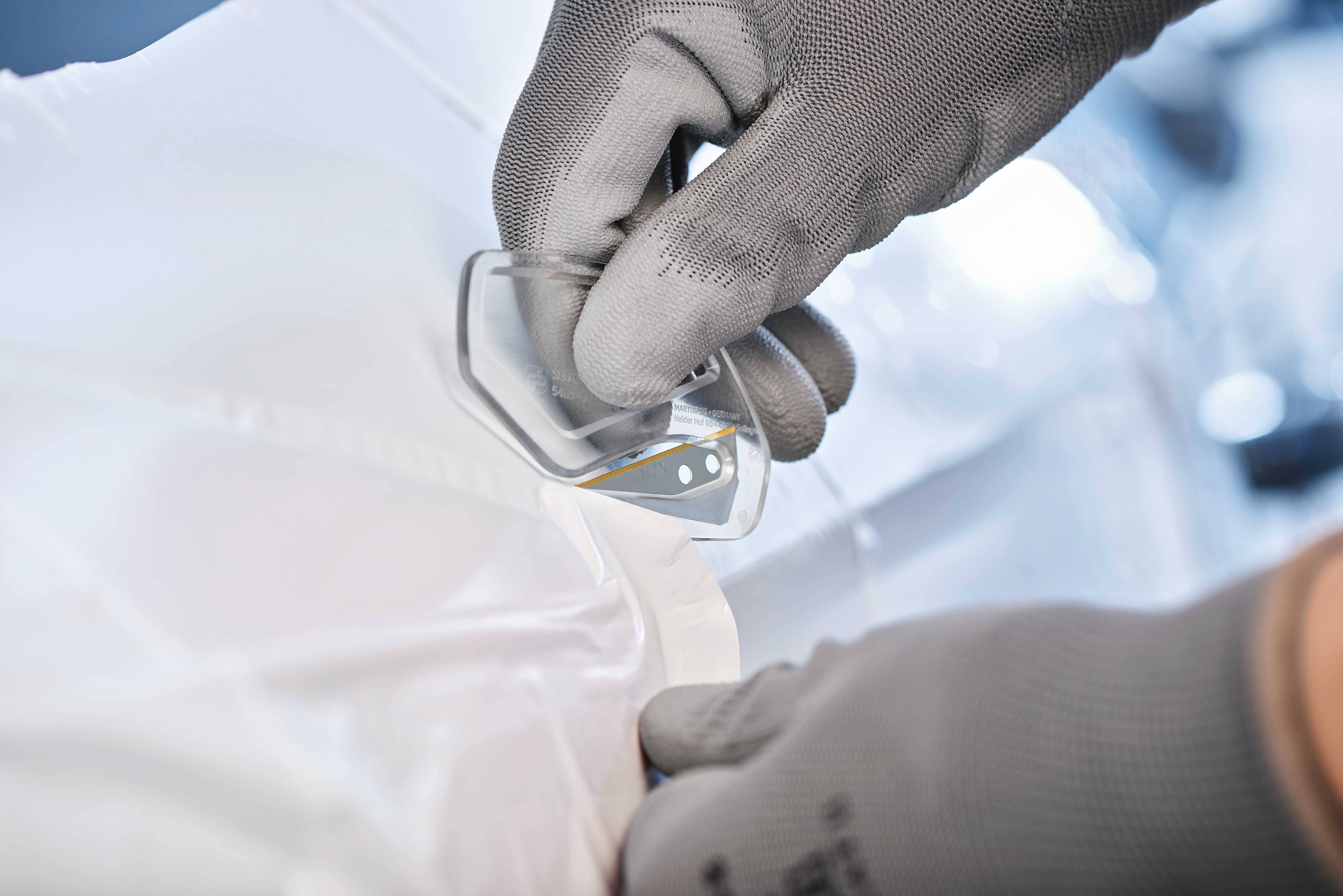 Dłoń w szarym rękawiczce trzyma kawałek tworzywa sztucznego na białej, błyszczącej powierzchni. Wygląda, jakby była częścią większego obiektu.