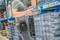 Osoba sortuje szare pojemniki z tworzywa sztucznego na regale magazynowym, ubrana w szarą koszulkę i czarne dżinsy, bez rozpoznawania twarzy.