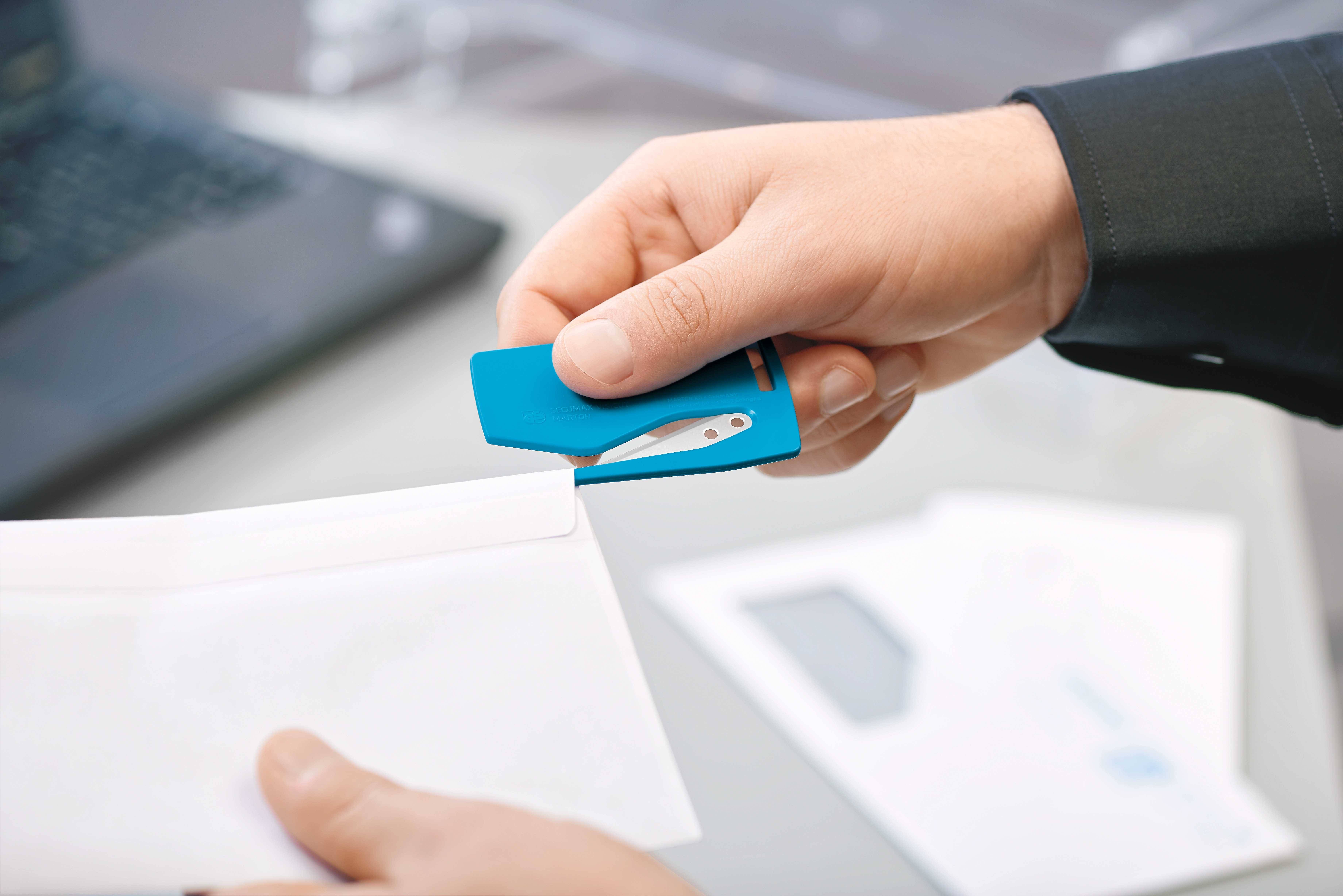 Dwie ręce otwierają biały list za pomocą niebieskiego noża do kopert, w tle nieostry laptop.