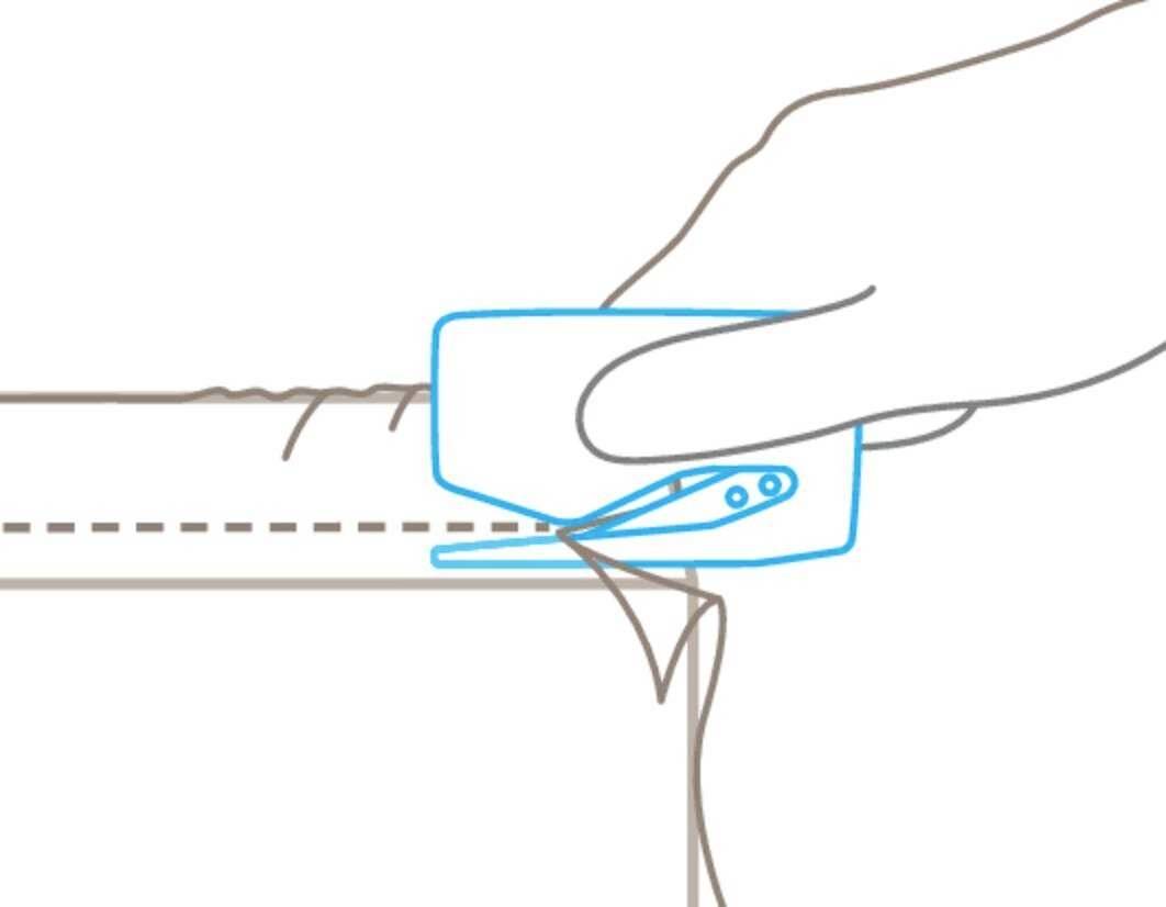 Ręka wycina wzdłuż linii przerywanej tkaninę specjalnym narzędziem oznaczonym na niebiesko.